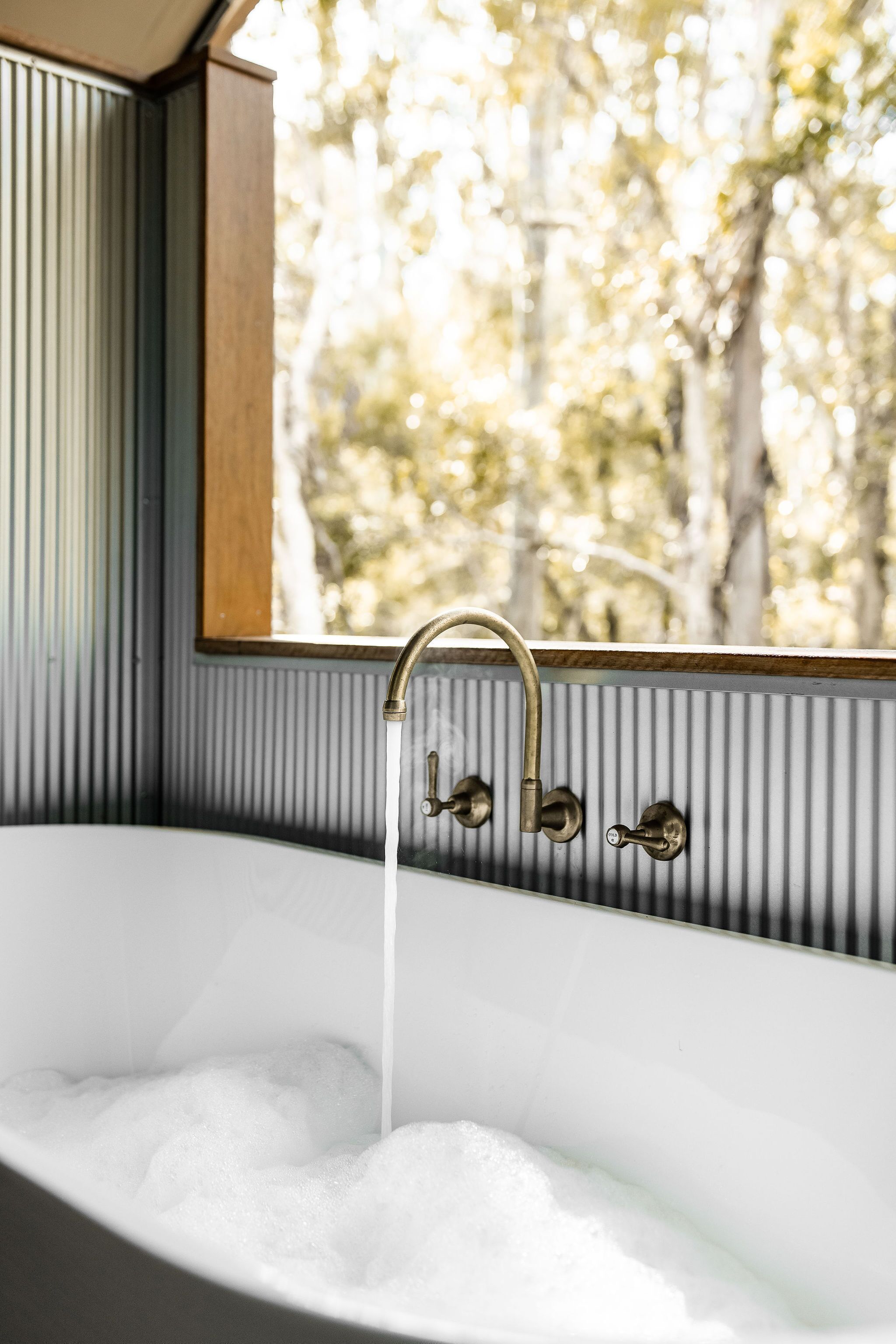Una bañera con agua corriente, una ventana con vistas a árboles y un marco de madera alrededor de la ventana.