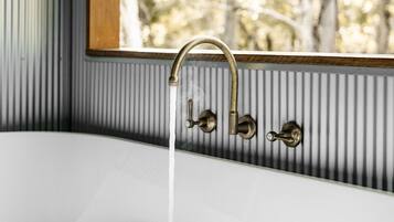 Una bañera con agua corriente, una ventana con vistas a árboles y un marco de madera alrededor de la ventana.