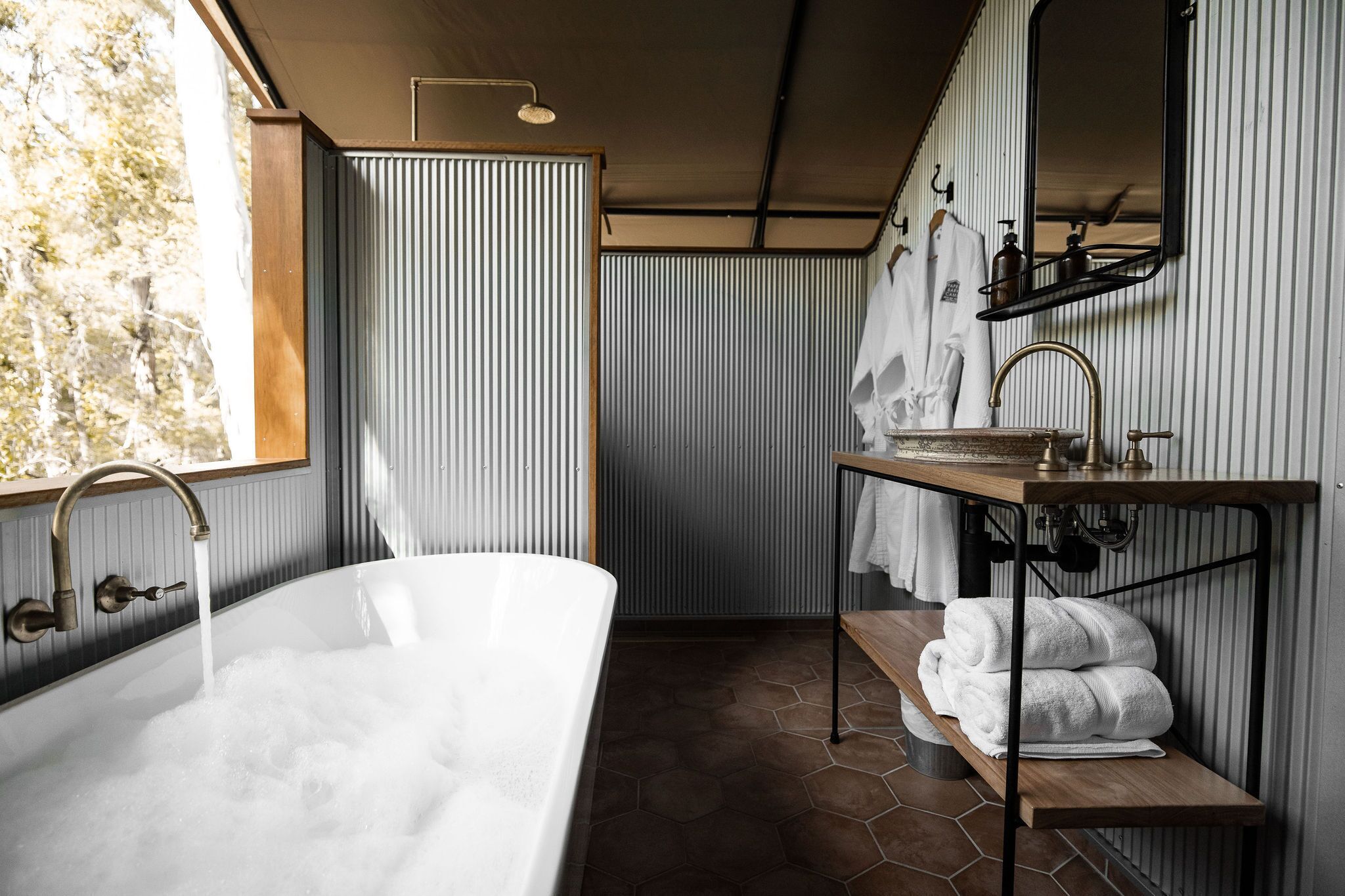 Un baño moderno con una bañera independiente, un mueble de tocador de madera con un espejo y toallas en un estante.