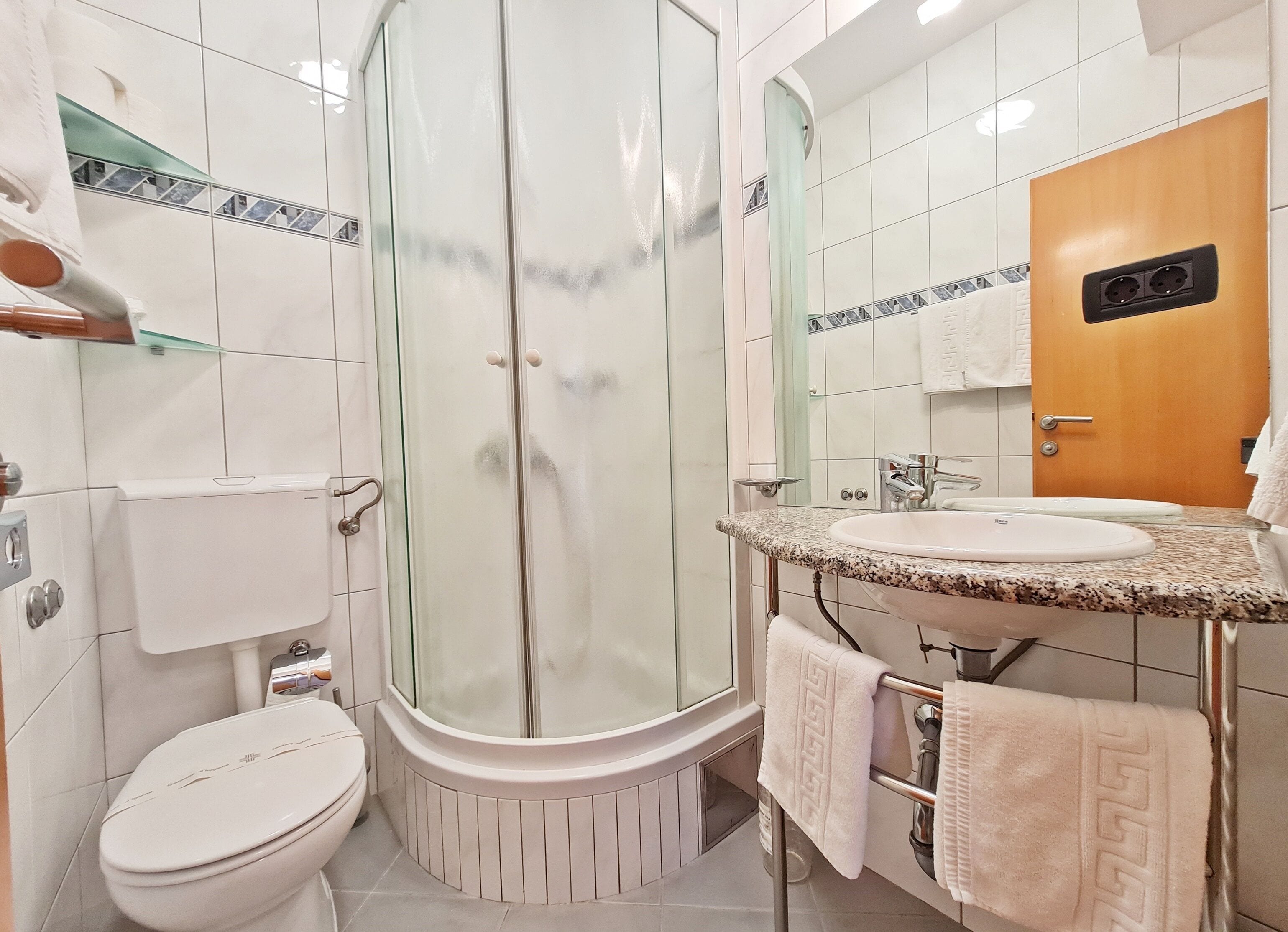 Un baño moderno con ducha envuelta en vidrio, inodoro y lavabo con tocador.