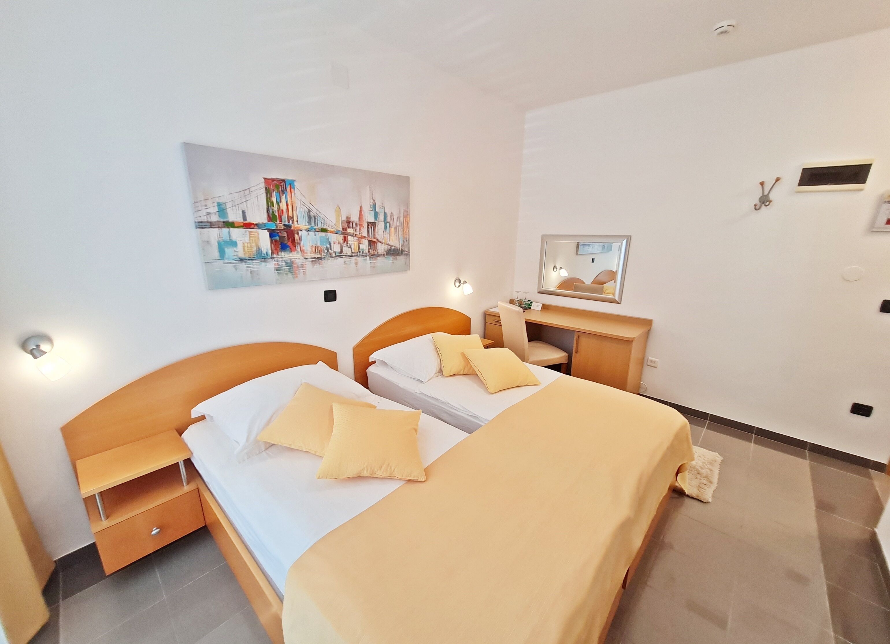Hotellihuone, jossa on kaksi sänkyä, työpöytä, tuoli, peili ja taulu seinällä.