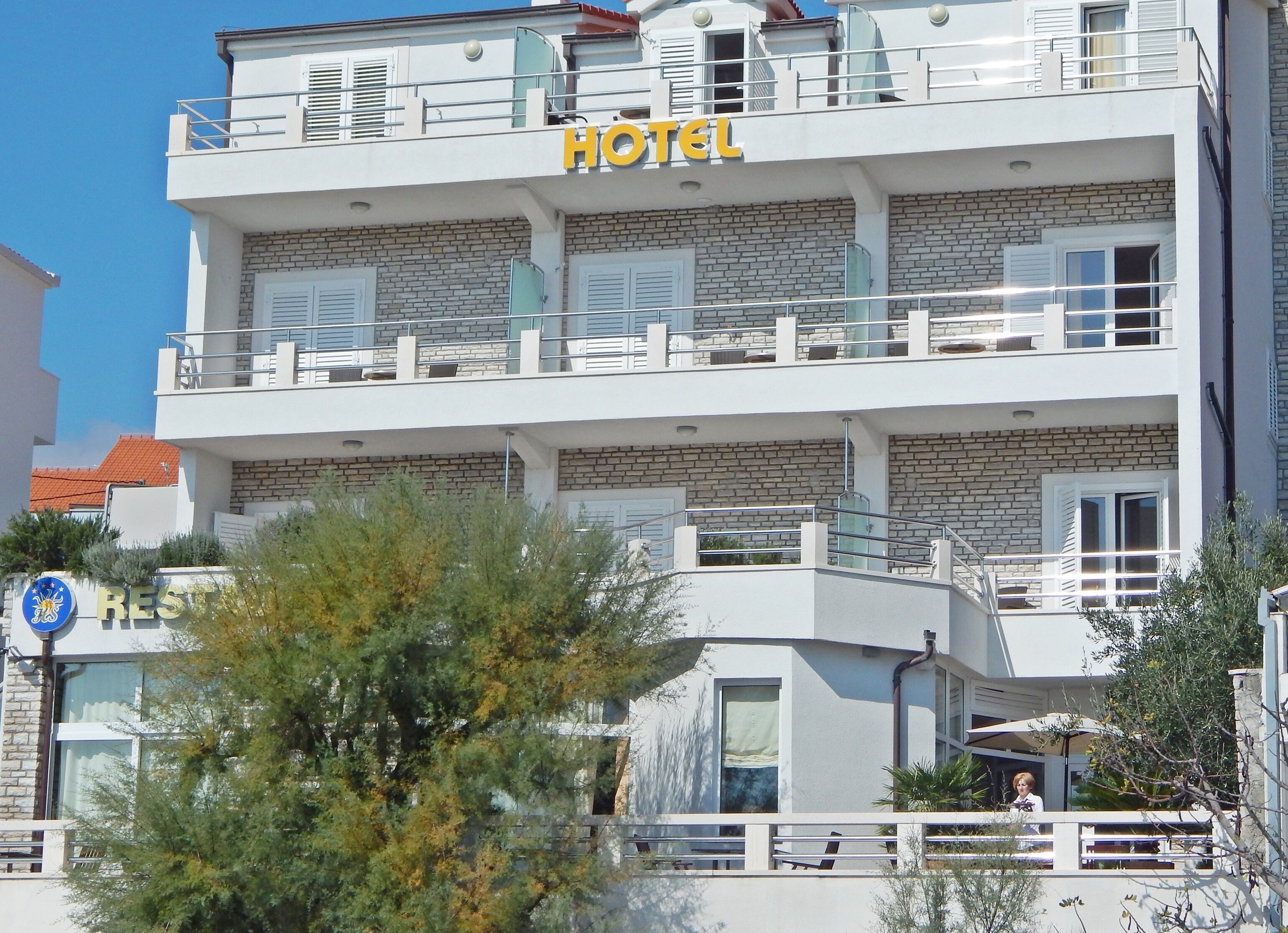 Un hotel de varios pisos con fachada de piedra, balcones y un cielo azul despejado.