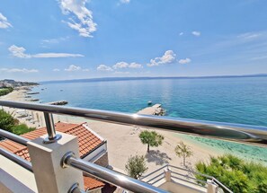 Vista costera desde un balcón, con cielo despejado, playa de arena y mar tranquilo.