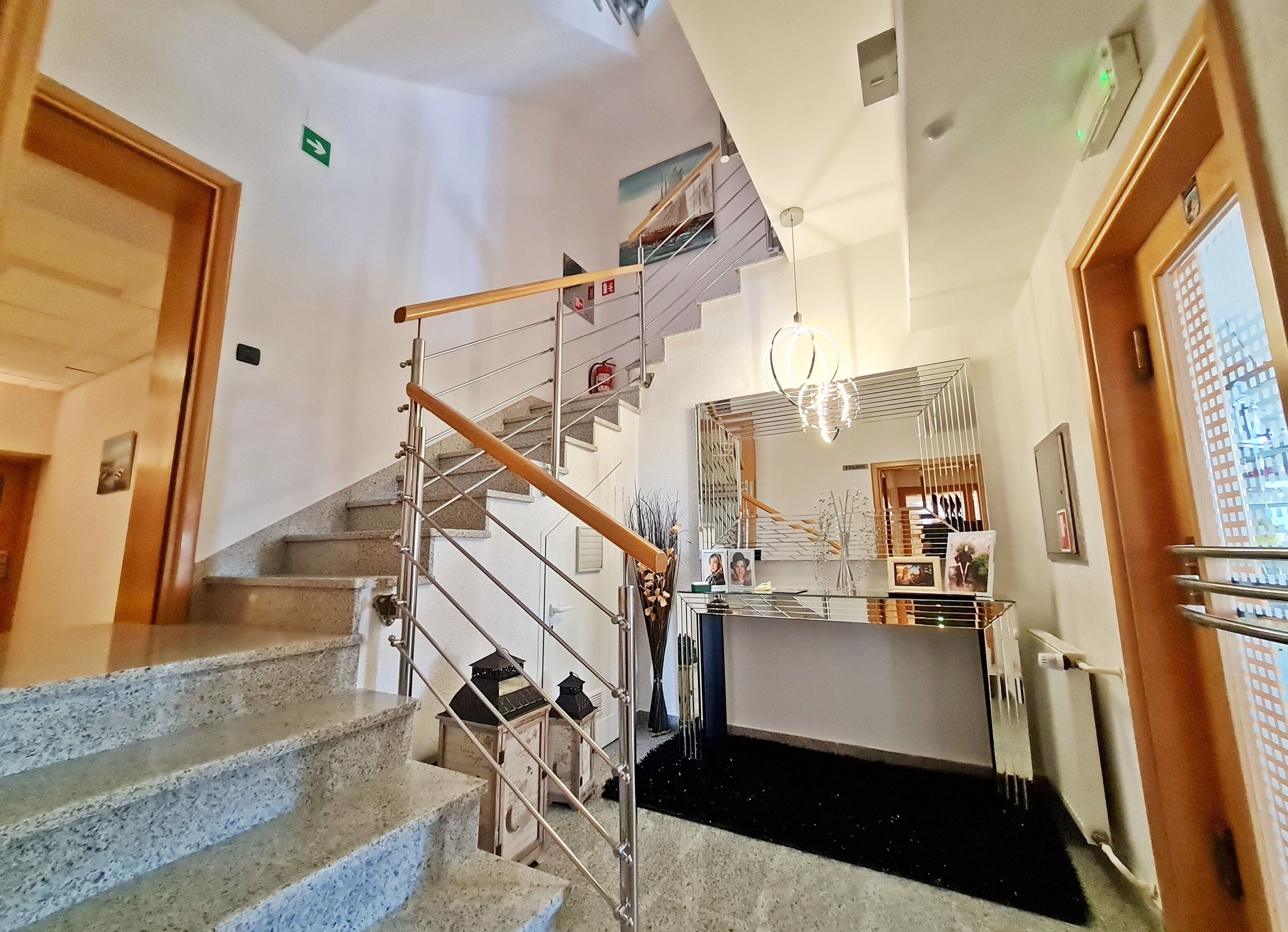 Un escalier doté d’une main courante en bois et de balustrades en métal, menant à un palier avec une cloison en verre et des tableaux encadrés.
