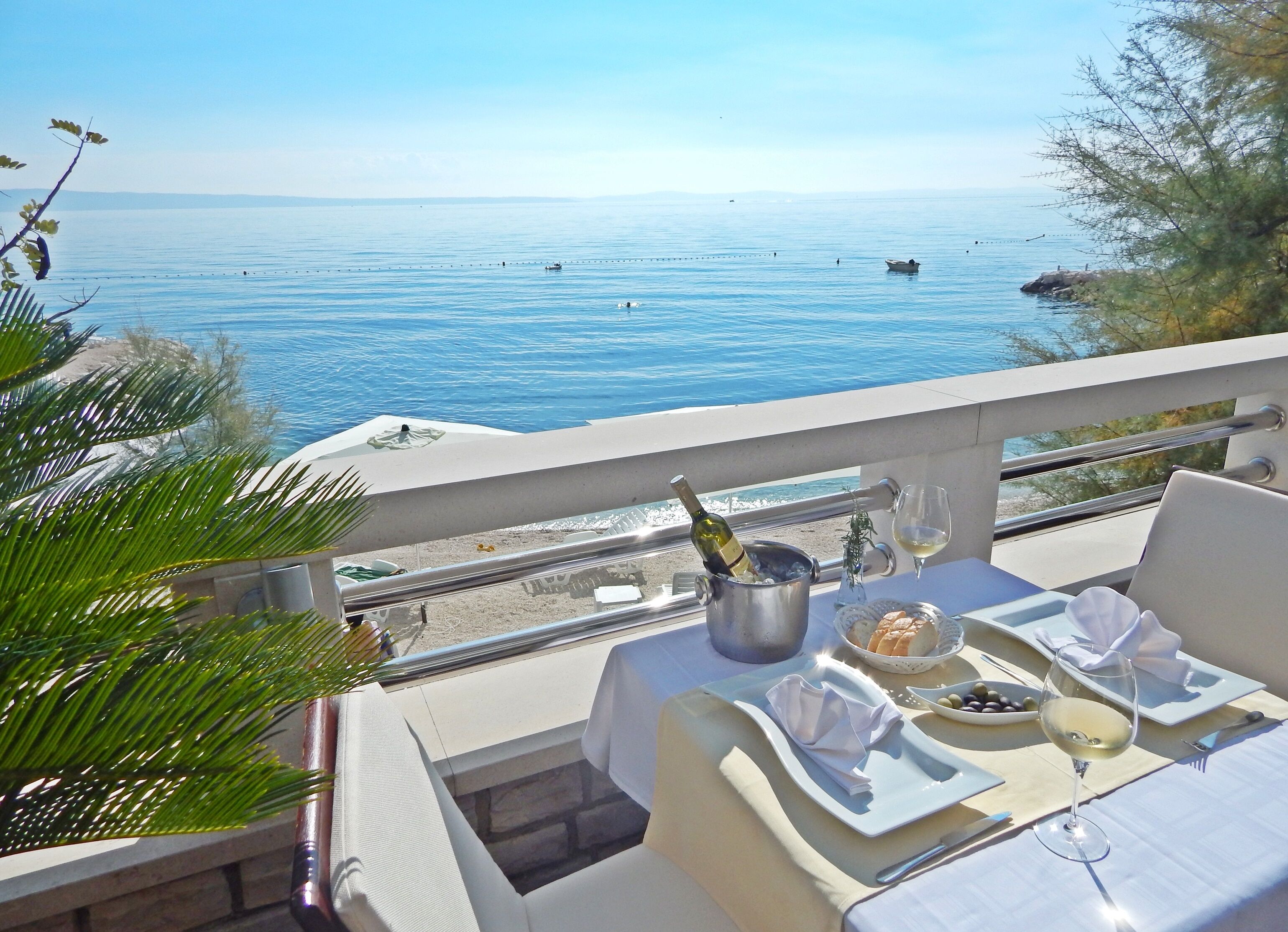 A terrace with a table set for two, overlooking a calm sea.