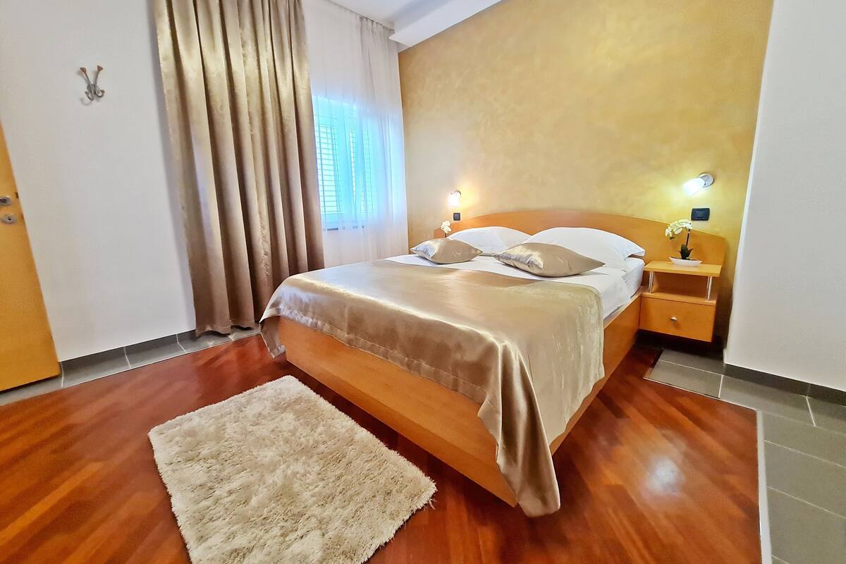 A neatly arranged bedroom with a bed, bedside tables, a nightstand, a rug, and a window with curtains.
