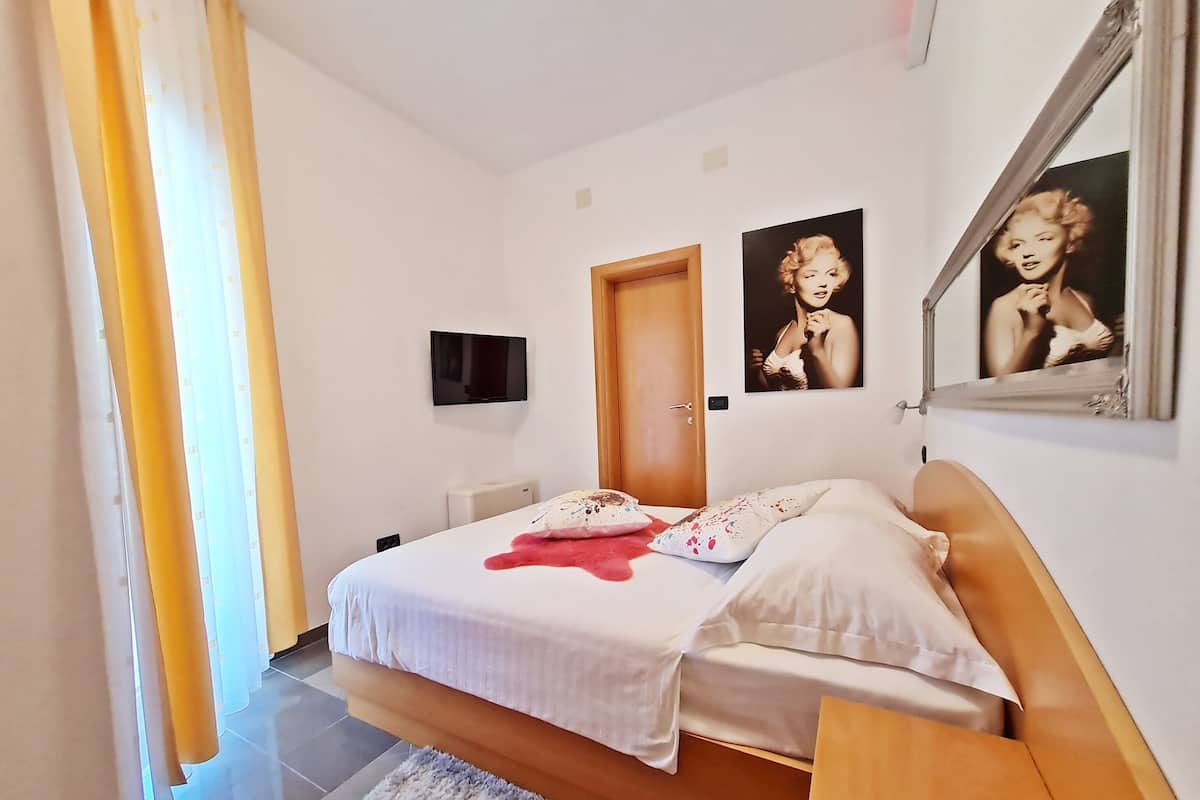 A bedroom with a bed, a TV, a door, and two framed pictures on the wall.