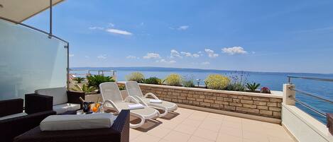 A balcony with wicker furniture, a glass partition, and a view of the sea.