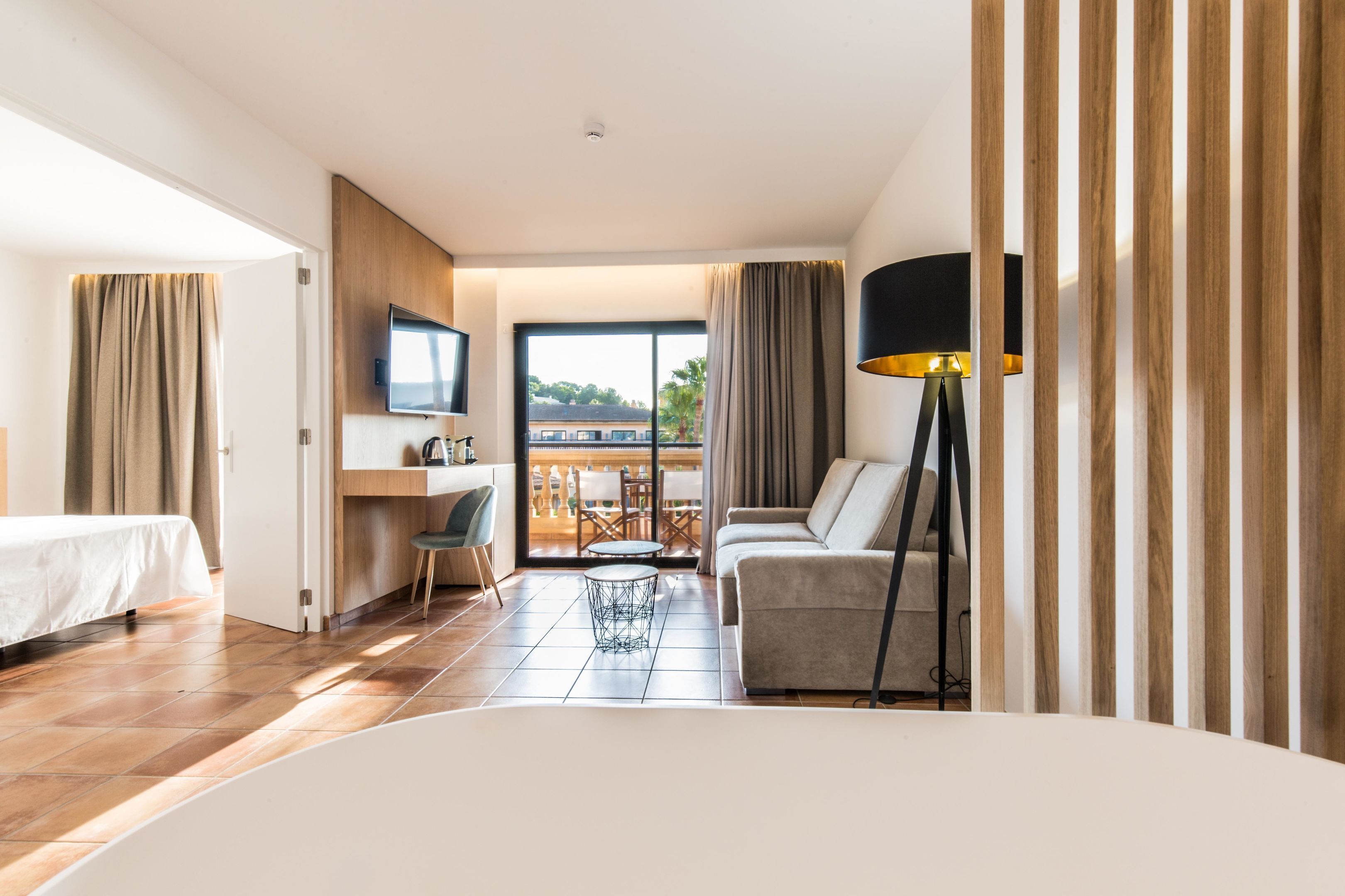 Habitación de hotel con cama, sofá, televisor, escritorio y balcón con vistas.
