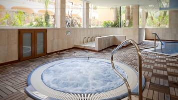 A hot tub area with a wooden deck, a seating area, and large windows with a view of greenery.