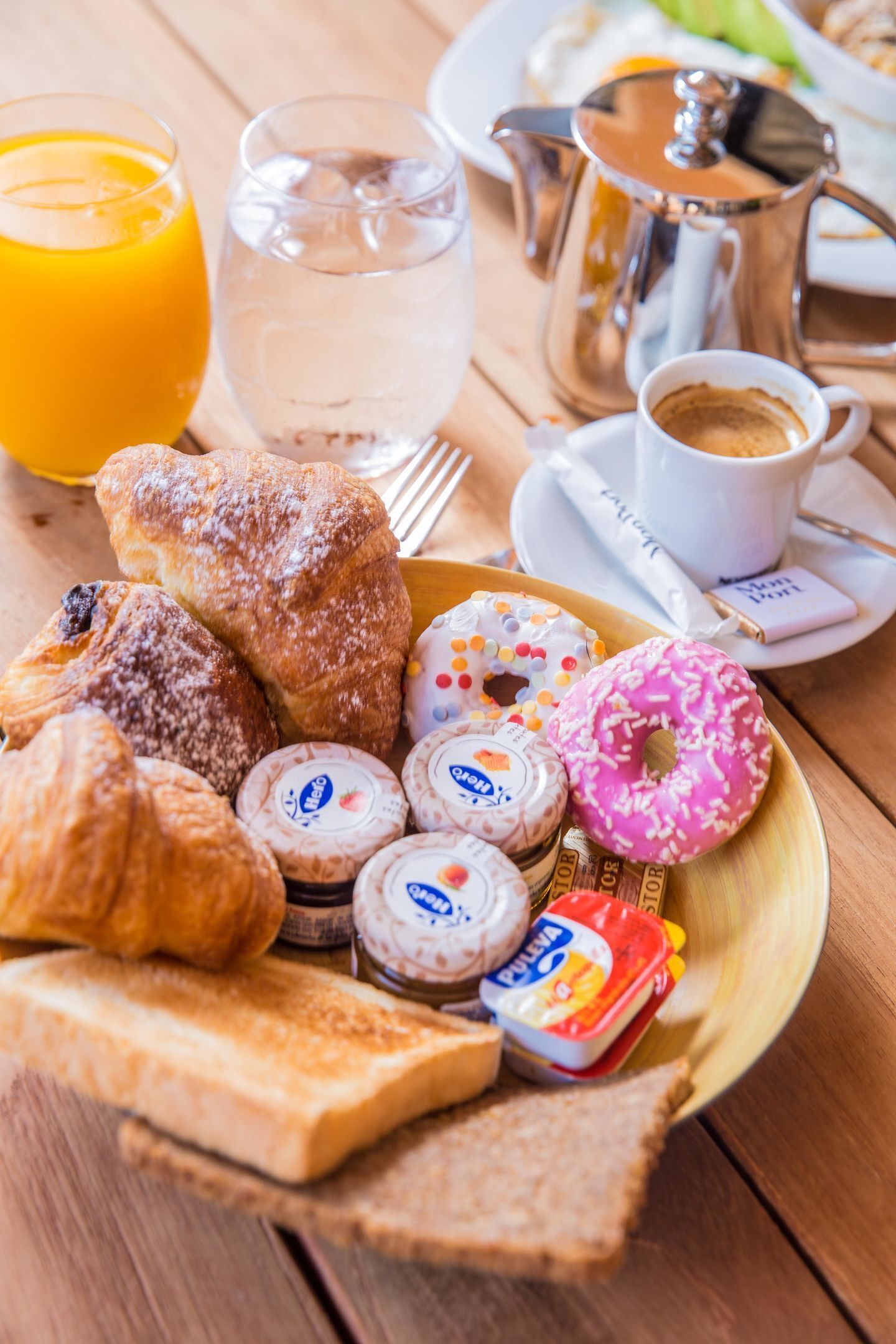Una bandeja de desayuno con bollos, un donut cubierto de glaseado rosa y una taza de café.