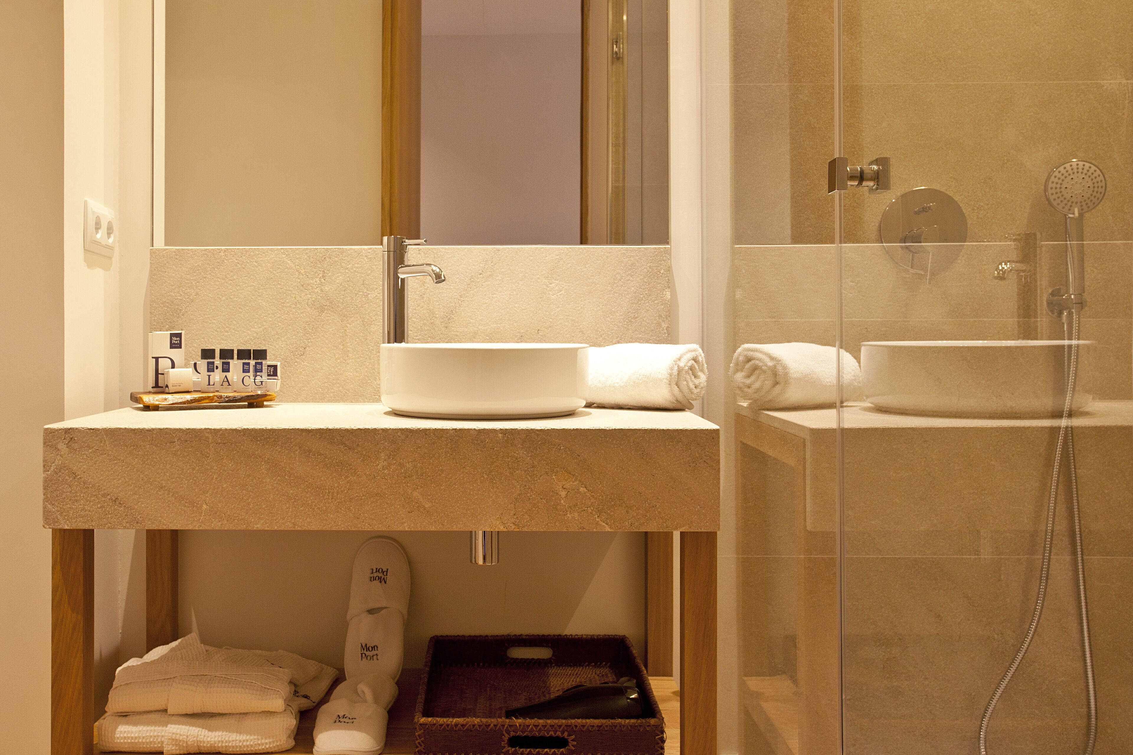 Une salle de bain avec un grand miroir, un lavabo et une douche. On peut voir des serviettes et un porte-chaussures.