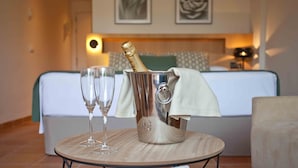 Une chambre avec un lit, une table de chevet sur laquelle se trouvent une bouteille de champagne et des verres, ainsi qu’un plateau de chocolats.