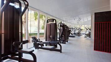 Un gimnasio con diversas máquinas de ejercicio, ventanas amplias y una zona roja para entrenar.