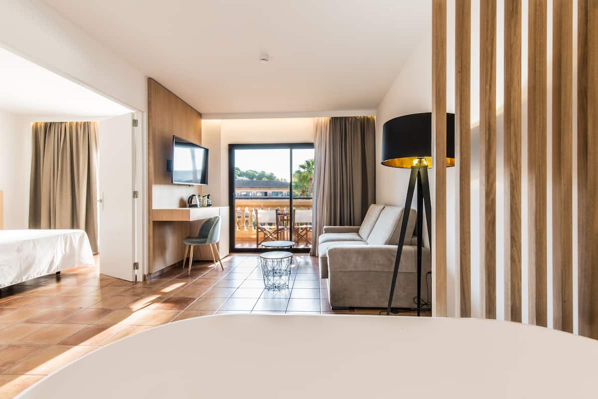 A hotel room with a bed, a desk, a chair, a sofa, and a balcony with a view.