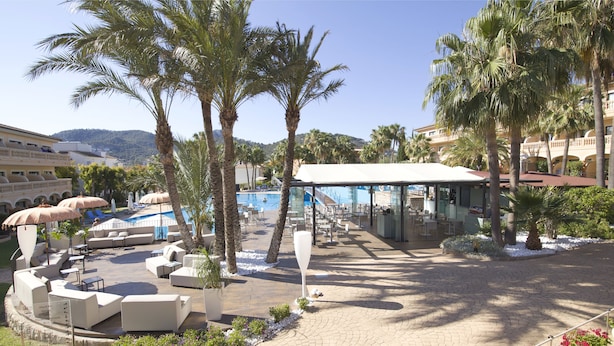 Un espace piscine aménagé dans un complexe hôtelier, avec des chaises longues, des parasols et un espace salon abrité.