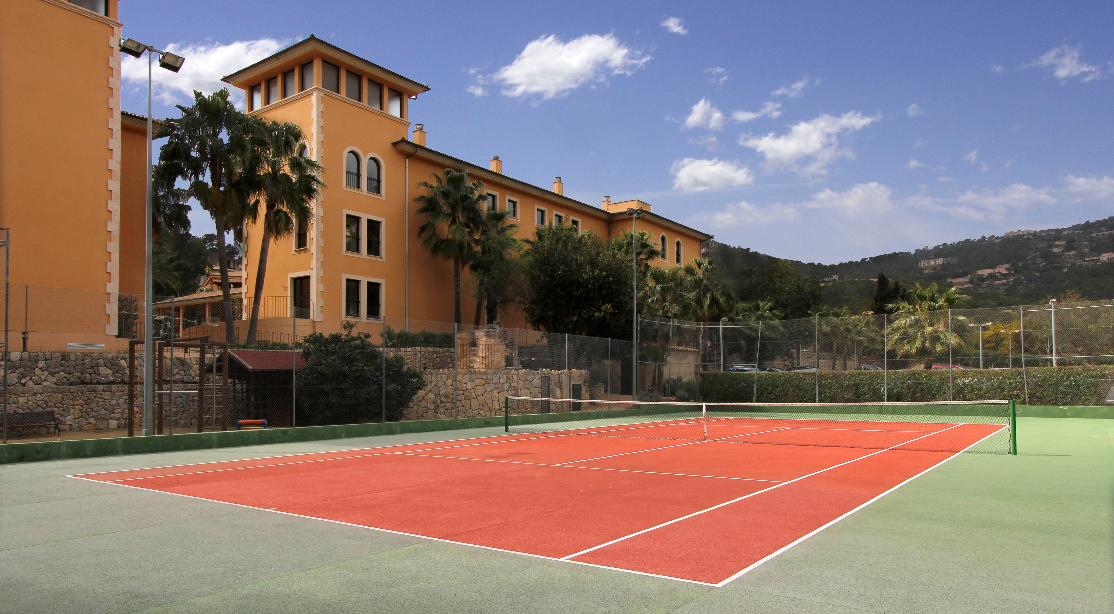 Een tennisbaan met een net, omringd door een hek en palmbomen.