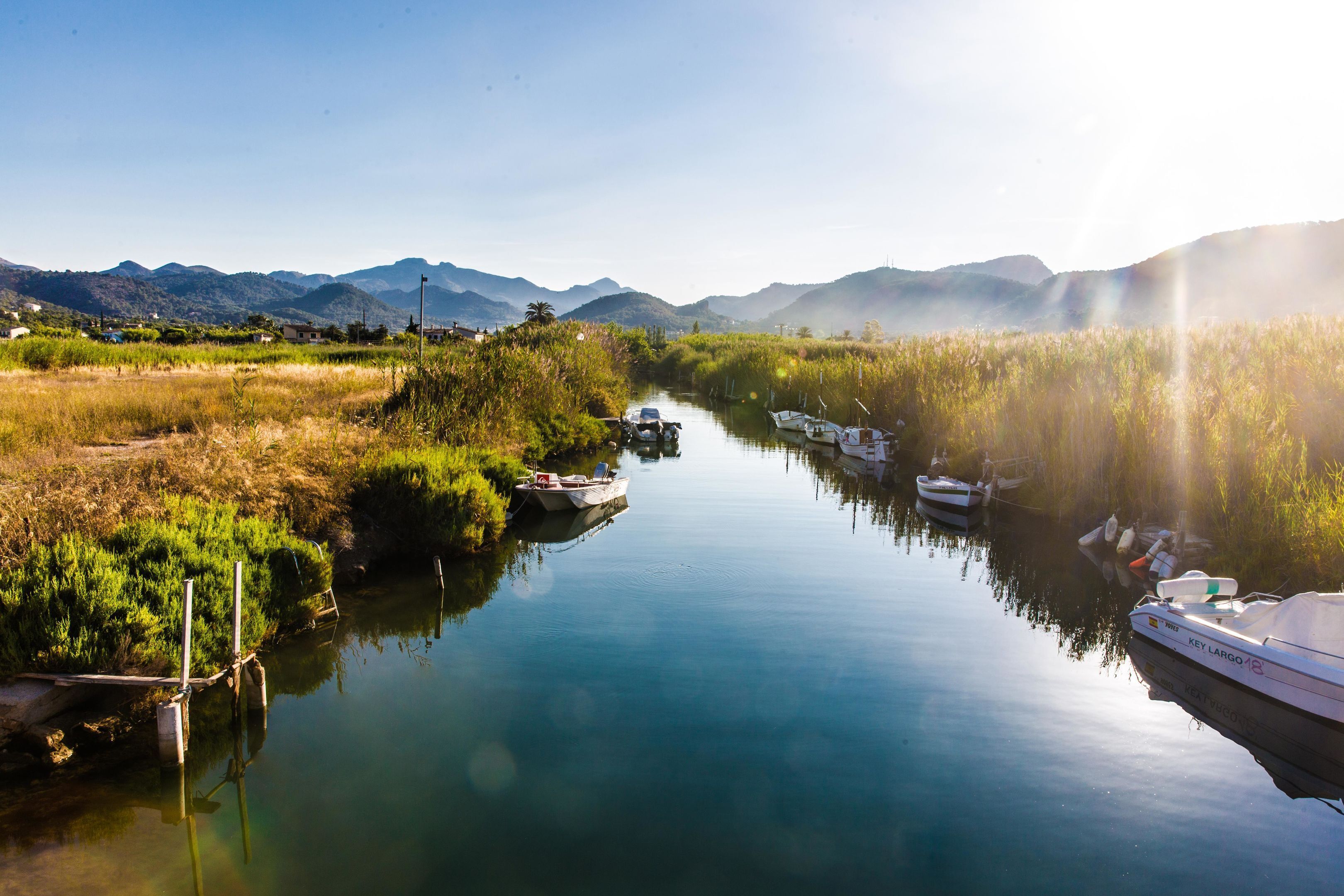 A calm river with boats, surrounded by greenery and mountains.