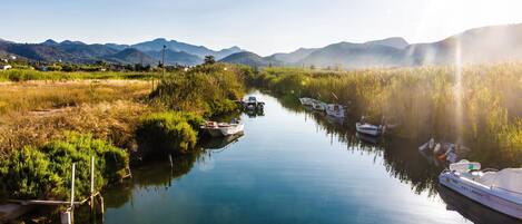 A calm river with boats, surrounded by greenery and mountains.