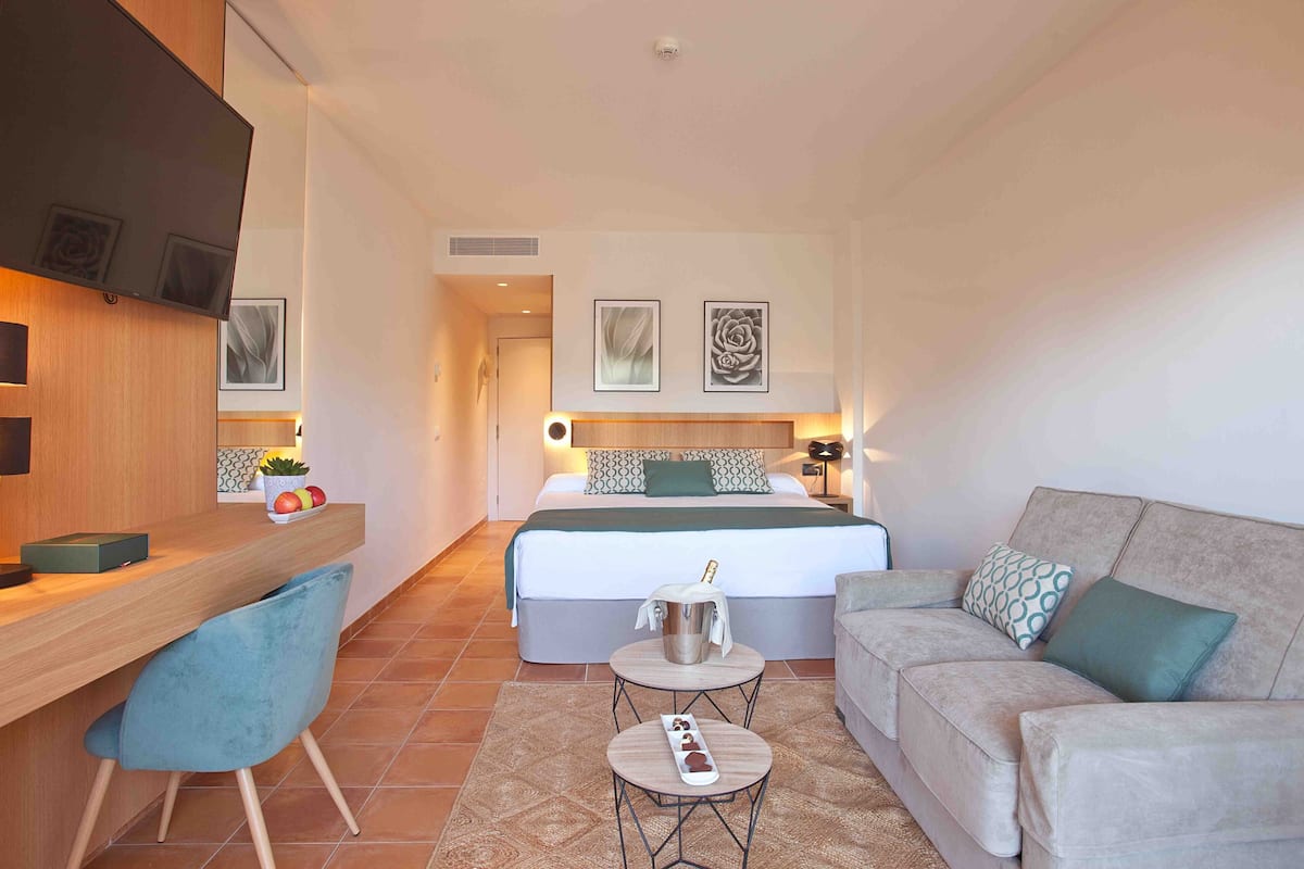 A hotel room with a bed, a sofa, a desk with a chair, and a small table.