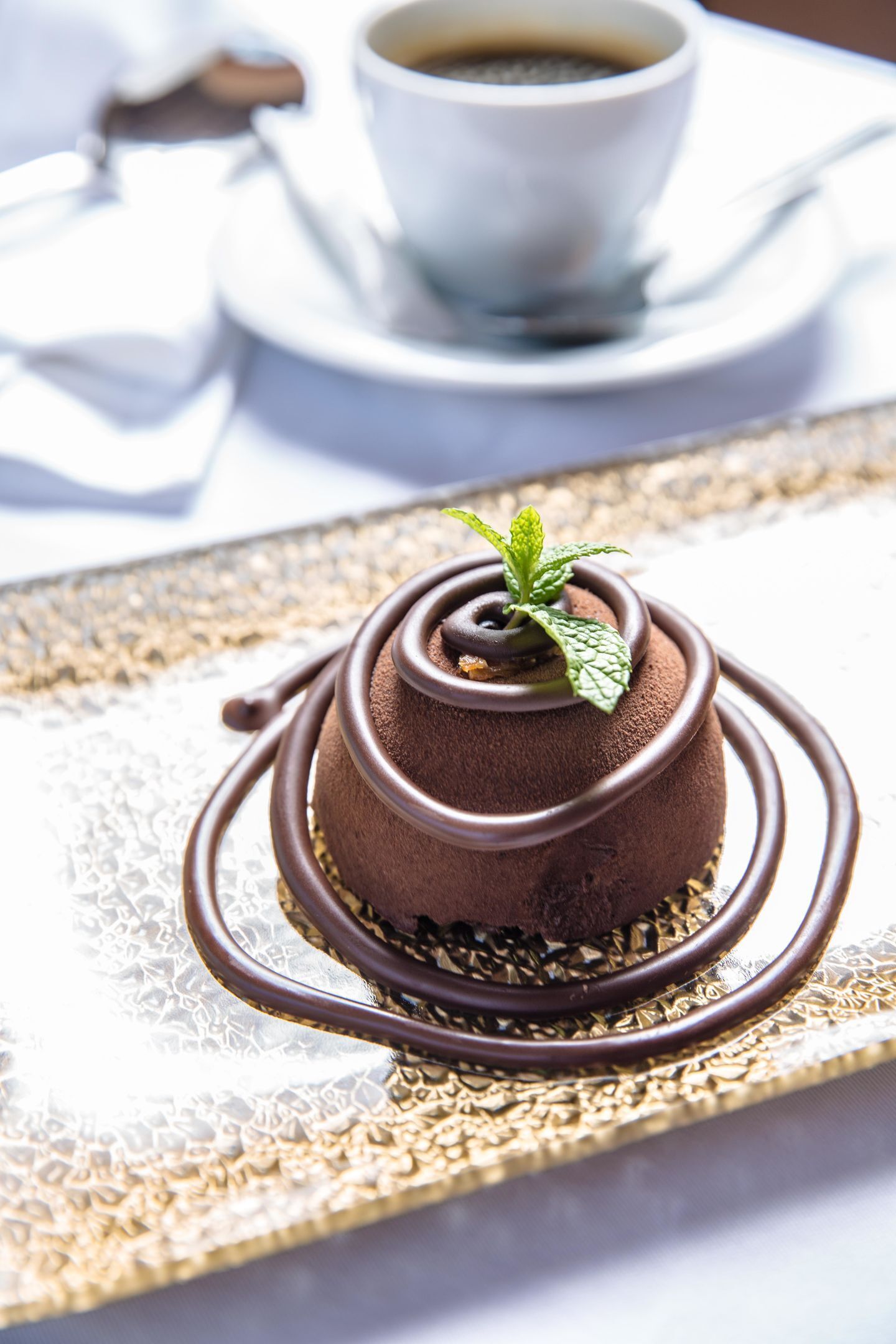 A dessert on a golden plate with a cup of coffee in the background.