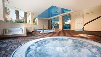 Un espace bien-être comprenant un jacuzzi, un fauteuil de massage et un plafond en verre.