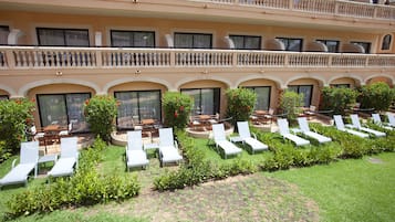 A hotel with multiple balconies, outdoor seating areas with tables and chairs, and a well-maintained lawn with sun loungers.