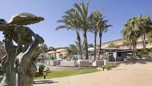 Une cour d’hôtel avec des palmiers, des sièges en plein air et une statue.
