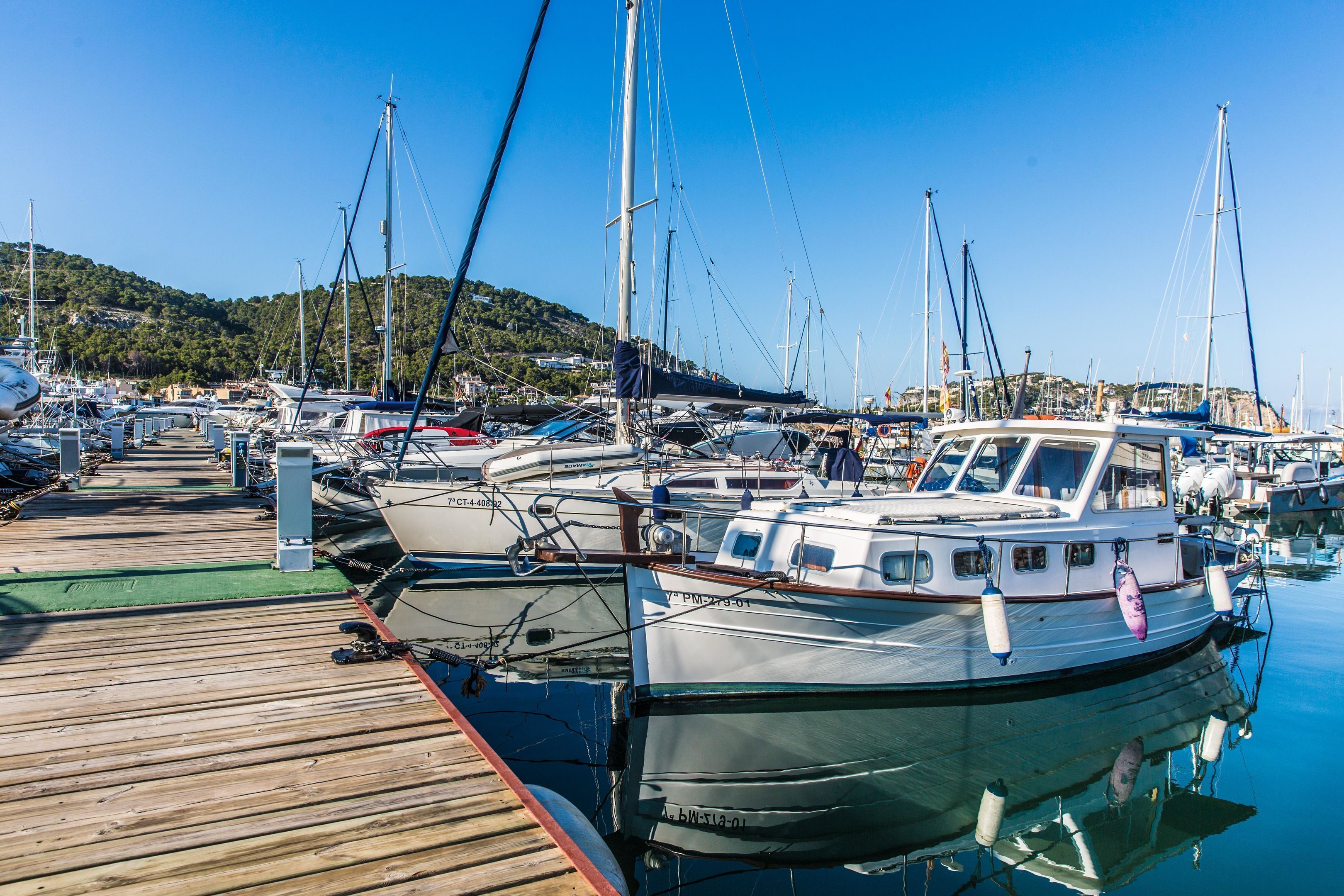 Un port de plaisance avec des bateaux amarrés, des passerelles en bois et un paysage vallonné en arrière-plan.