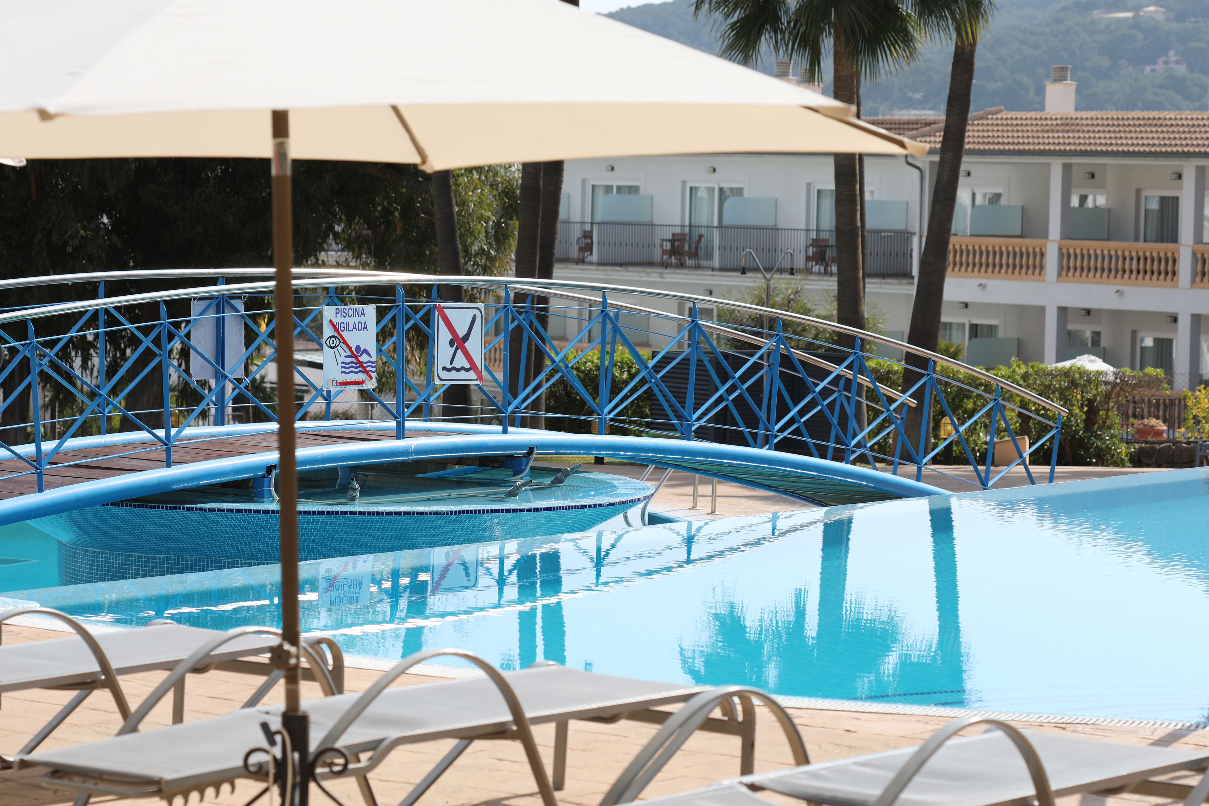 Una piscina con un puente metálico azul, sillas de descanso y un letrero que indica que no se permite nadar.