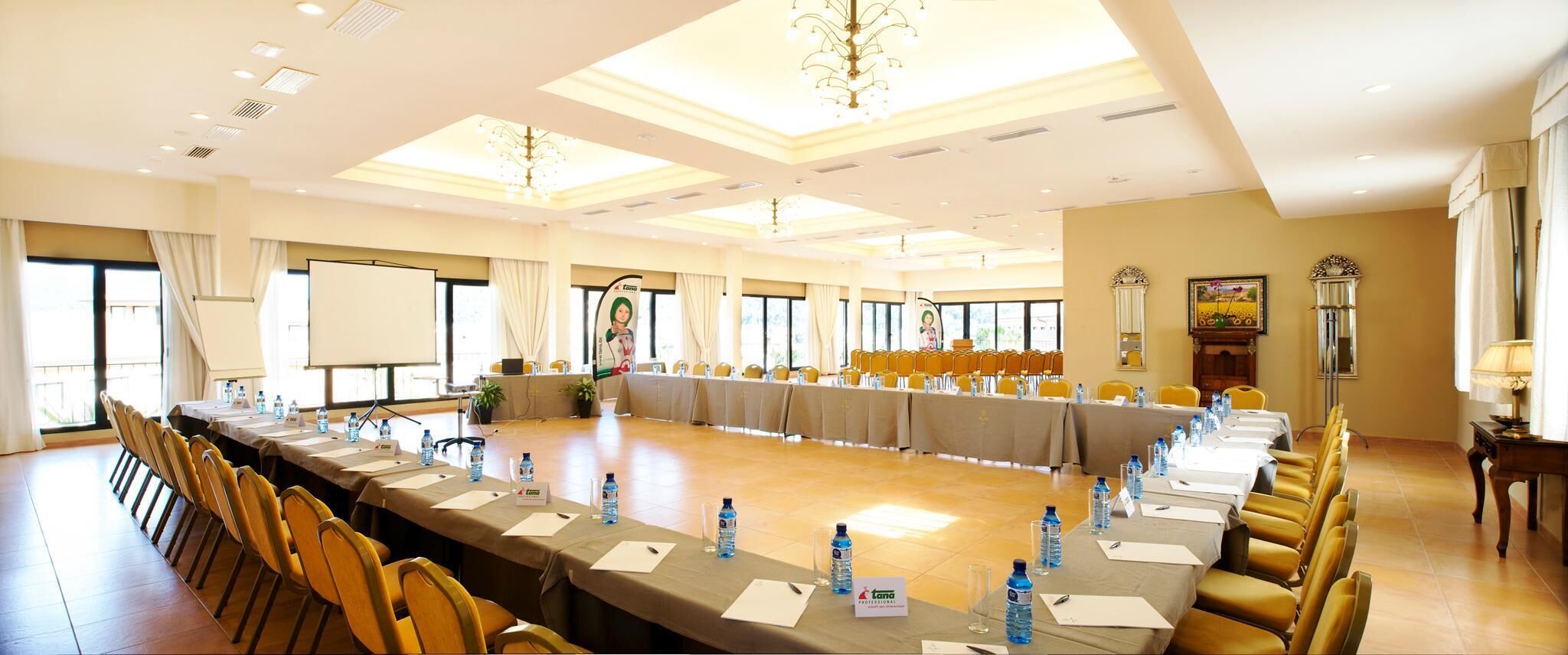A conference room with a long table, chairs, water bottles, nameplates, and a projector screen.