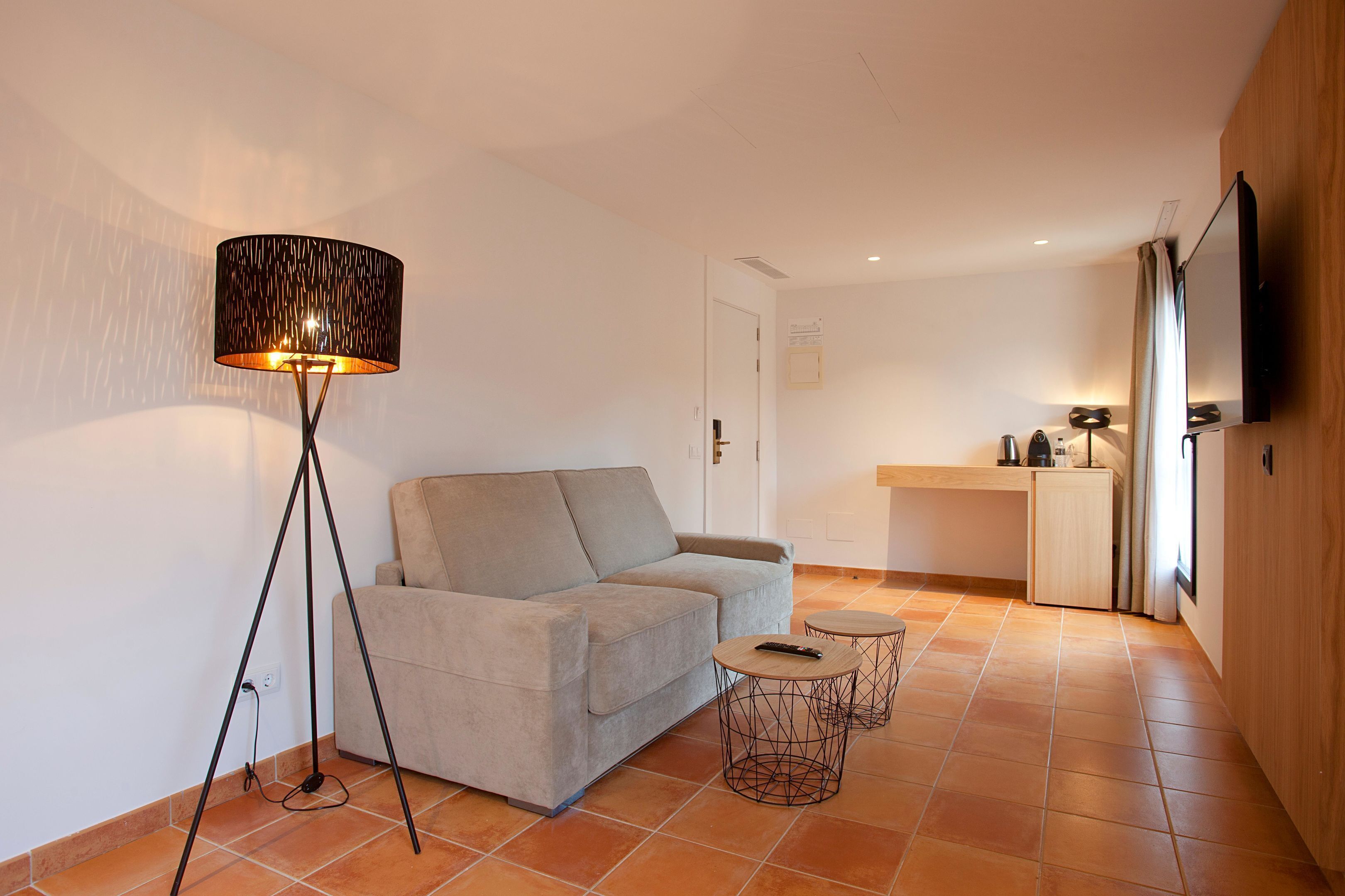 Un espace de vie comprenant un canapé, une lampe sur pied, deux tables d’appoint et un coin cuisine avec un comptoir et des placards.