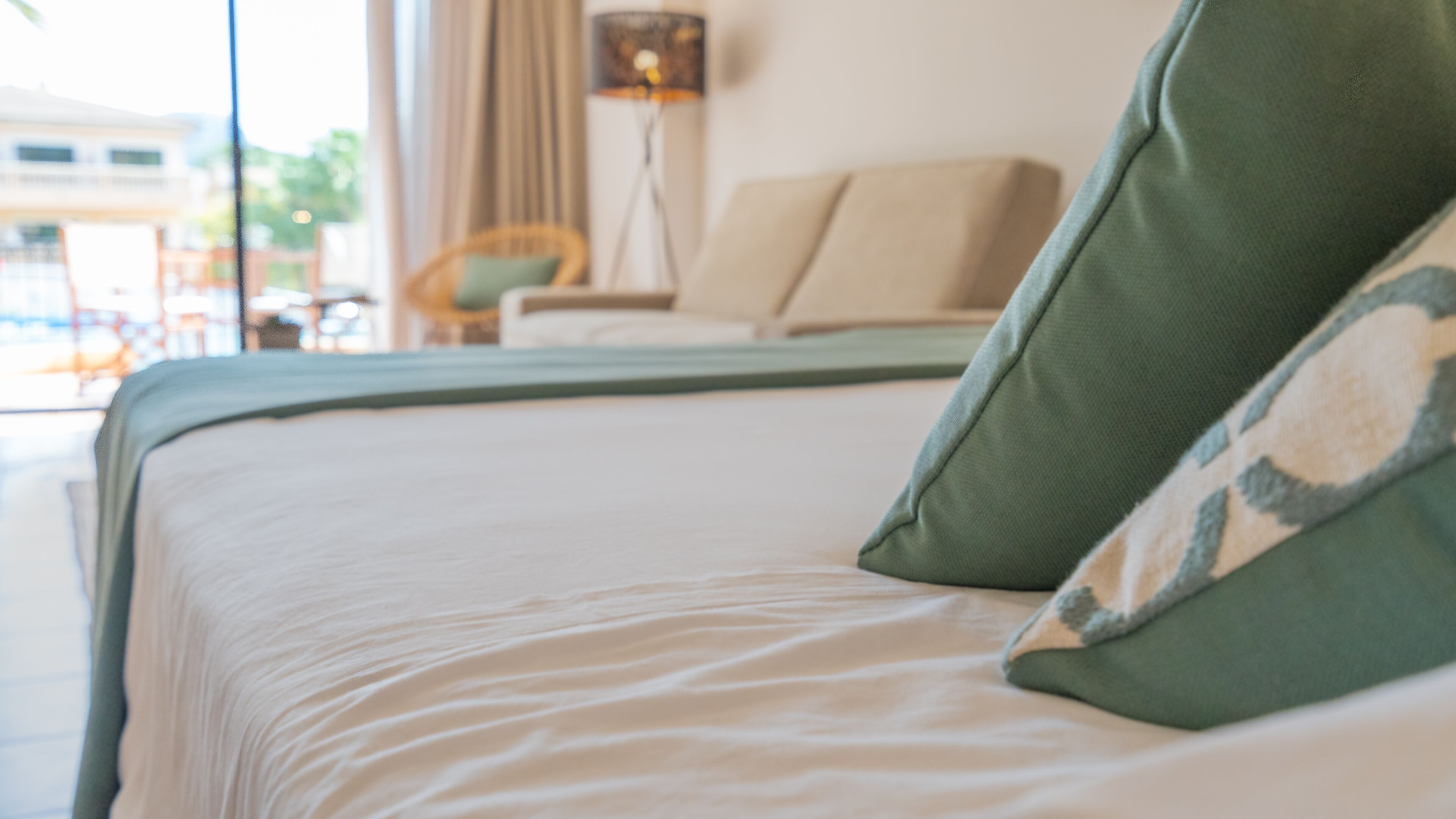 Una cama con un almohadón verde y una colcha blanca.