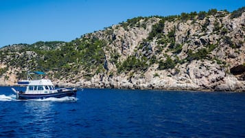 Un barco en un mar azul y transparente, con una costa rocosa y vegetación al fondo.