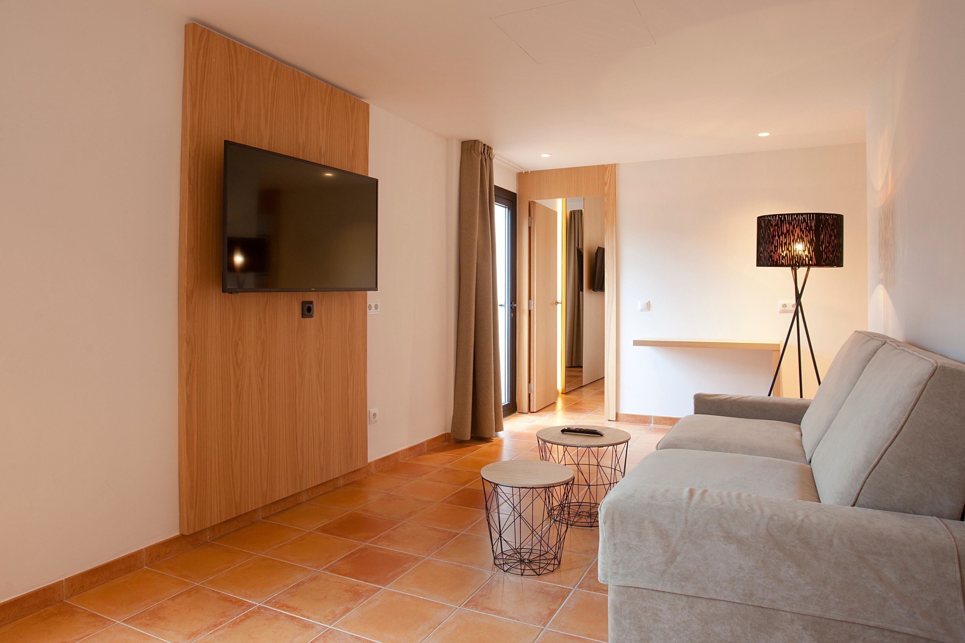 Una sala de estar moderna con un televisor de pantalla plana, un sofá, una mesita de centro y una lámpara de pie.