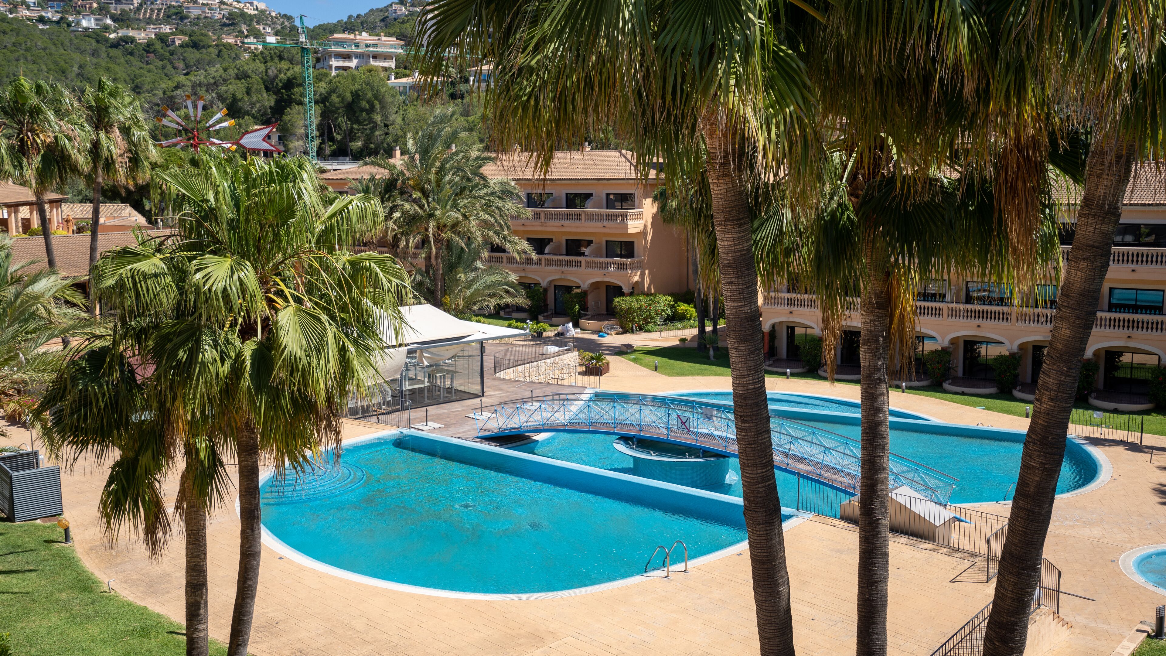 Una amplia piscina exterior rodeada de palmeras, con un edificio al fondo.