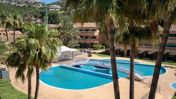 Una amplia piscina exterior rodeada de palmeras, con un edificio al fondo.