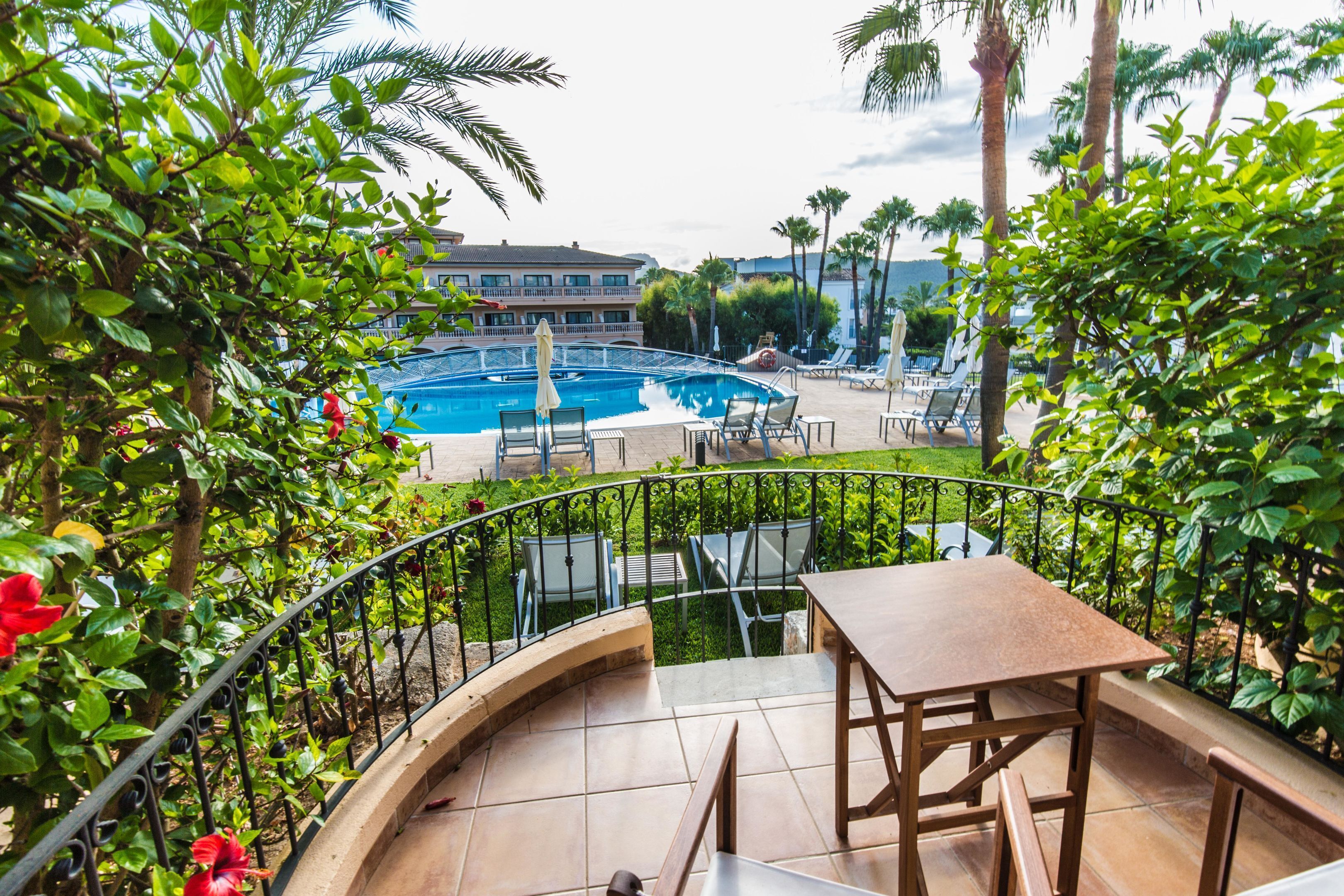 Un área de piscina con una mesa y sillas, rodeada de vegetación y un edificio al fondo.