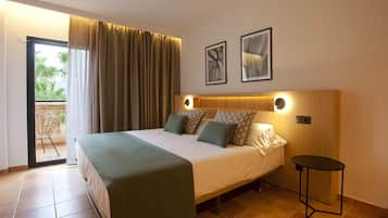 Habitació d'hotel amb un llit, una taula petita, un balcó amb una cadira i dos quadres a la paret.