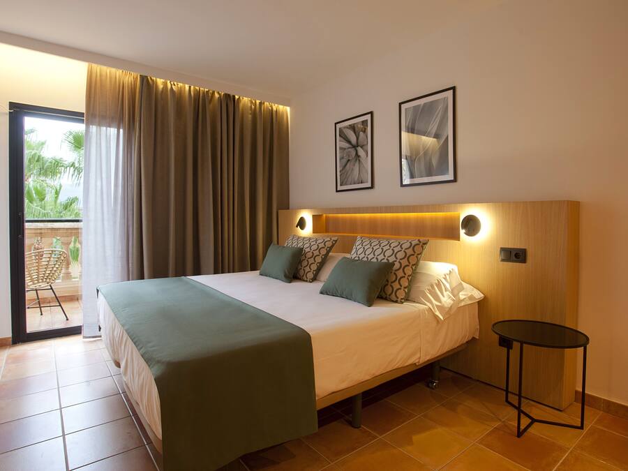 Habitació d'hotel amb un llit, una taula petita, un balcó amb una cadira i dos quadres a la paret.