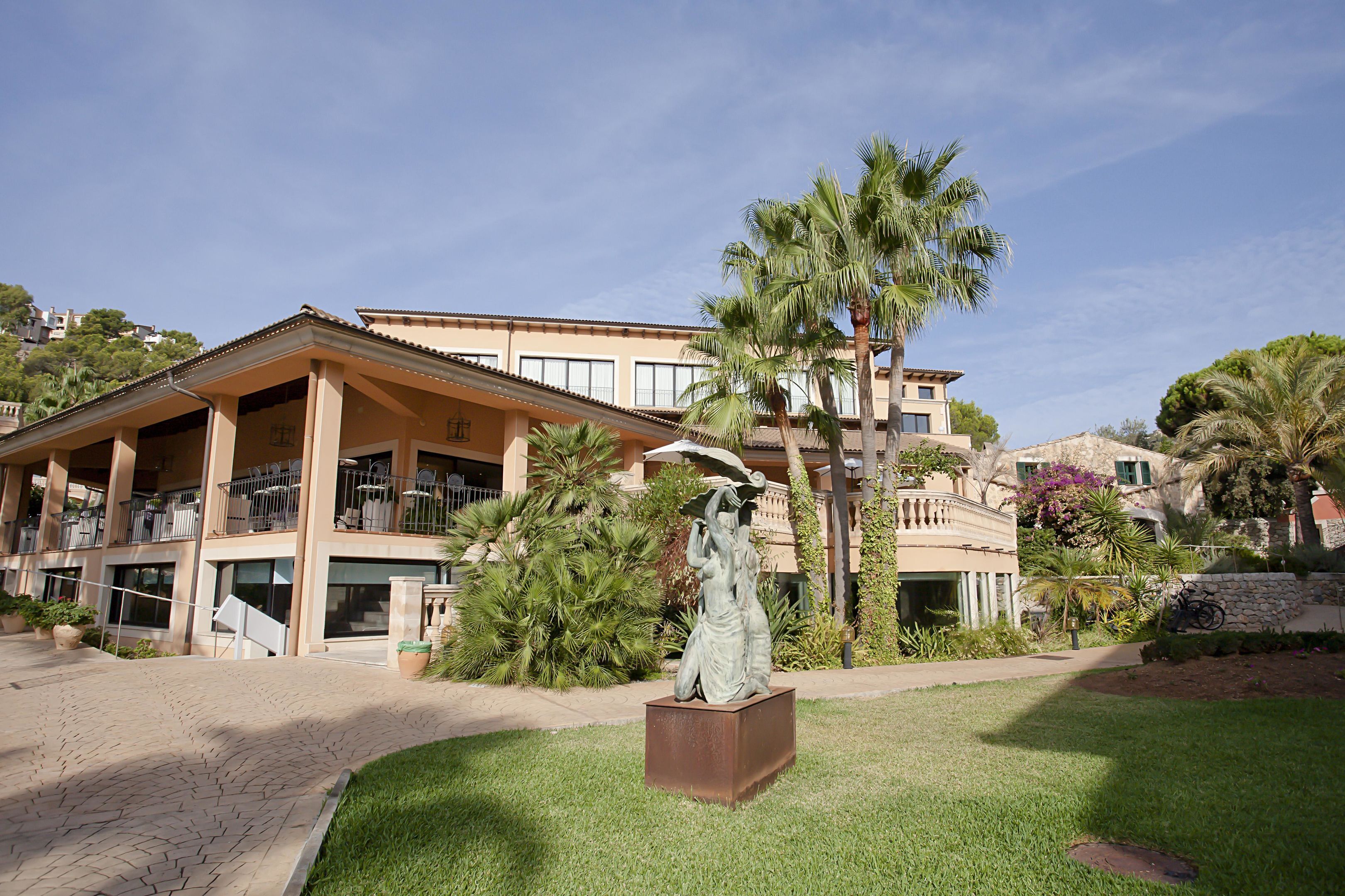 A building with a balcony, palm trees, and a statue in the foreground.