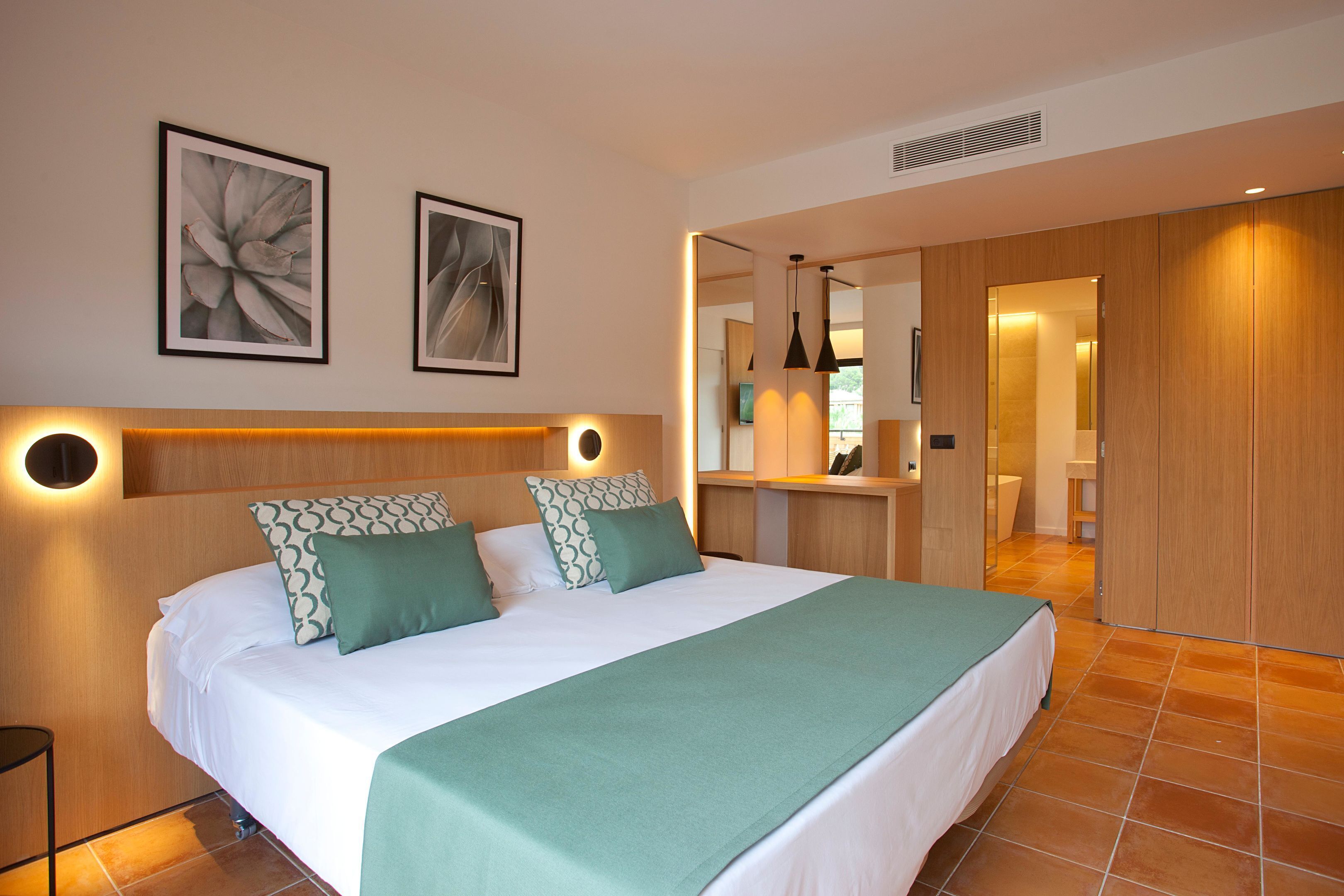 Un dormitorio moderno con una cama grande, dos luces fijadas a la pared y un espejo sobre la cama.
