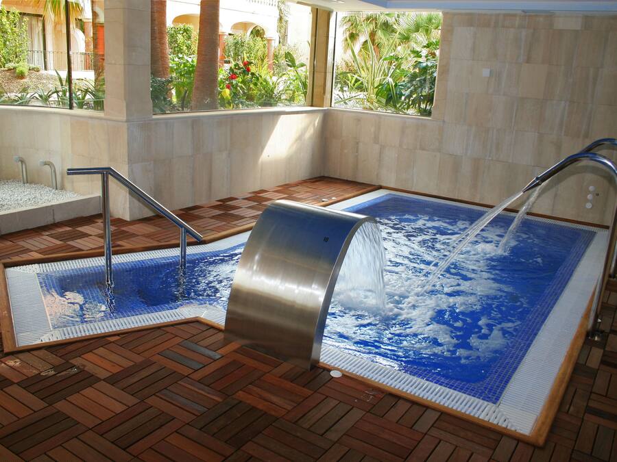 Un jacuzzi con suelo de madera, vista a follaje exterior y pared de azulejos.