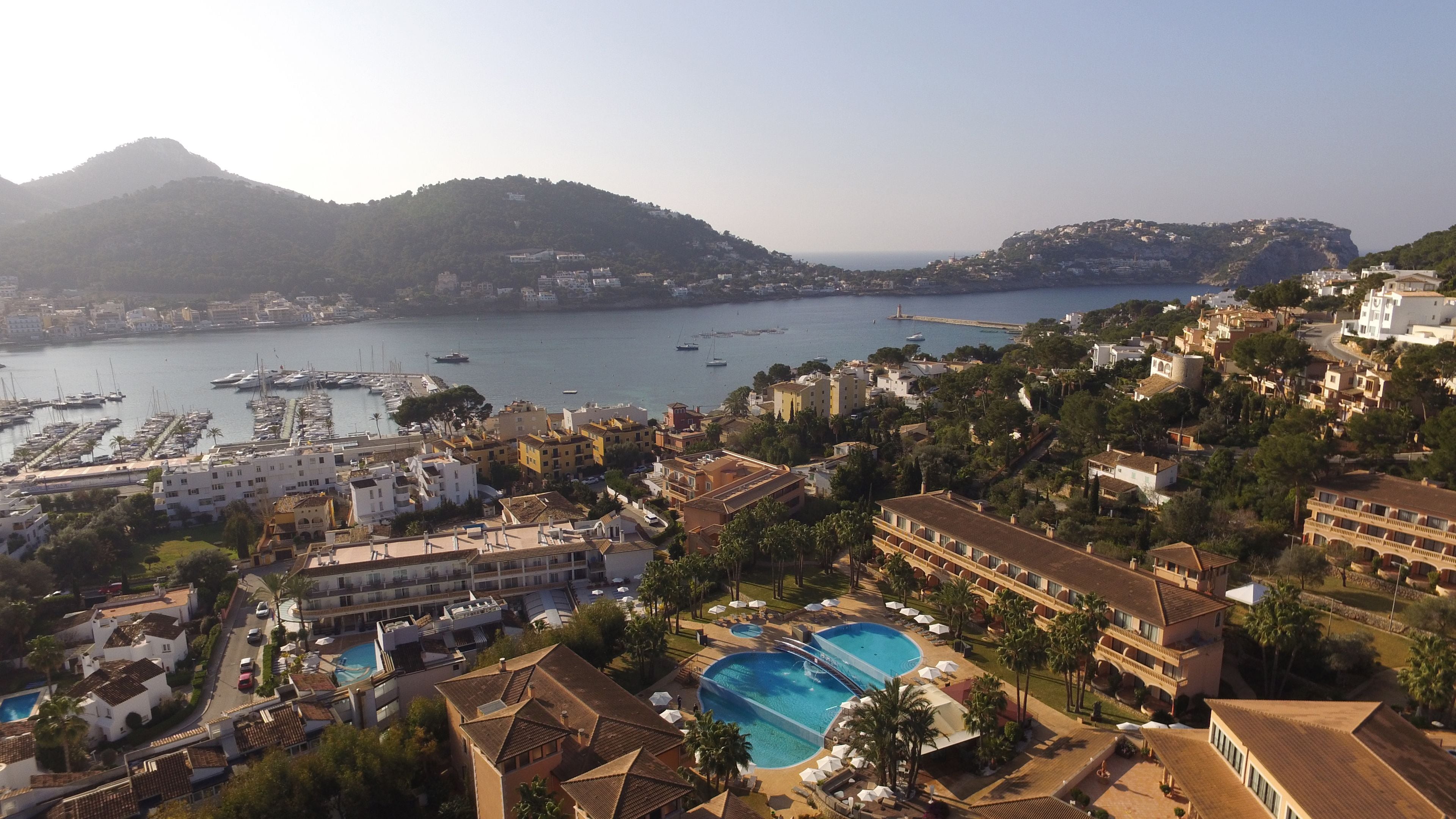 A coastal town with a marina, a large hotel with a pool, and mountainous terrain in the background.