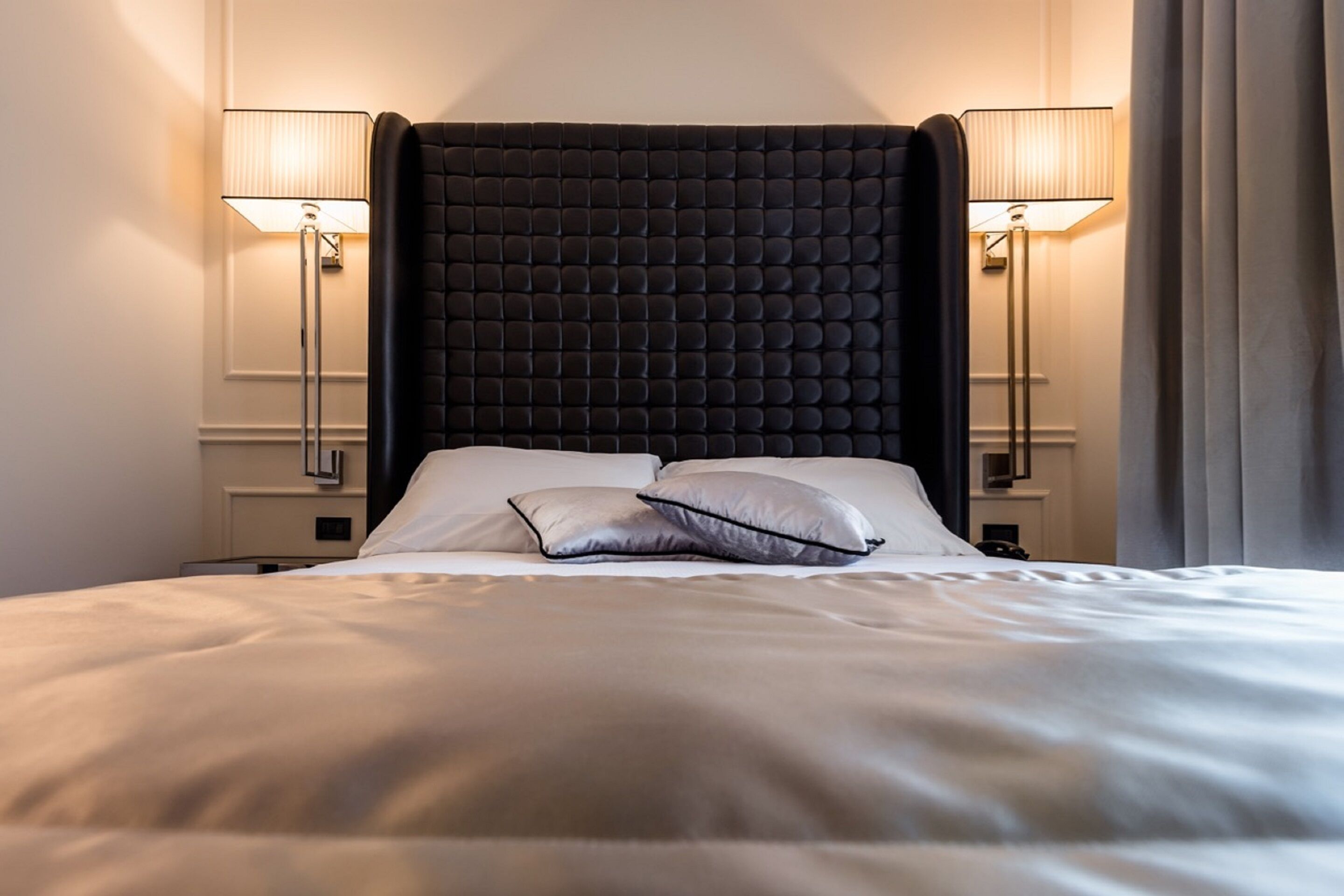 A hotel room with a large bed, two bedside lamps, and a dark headboard.