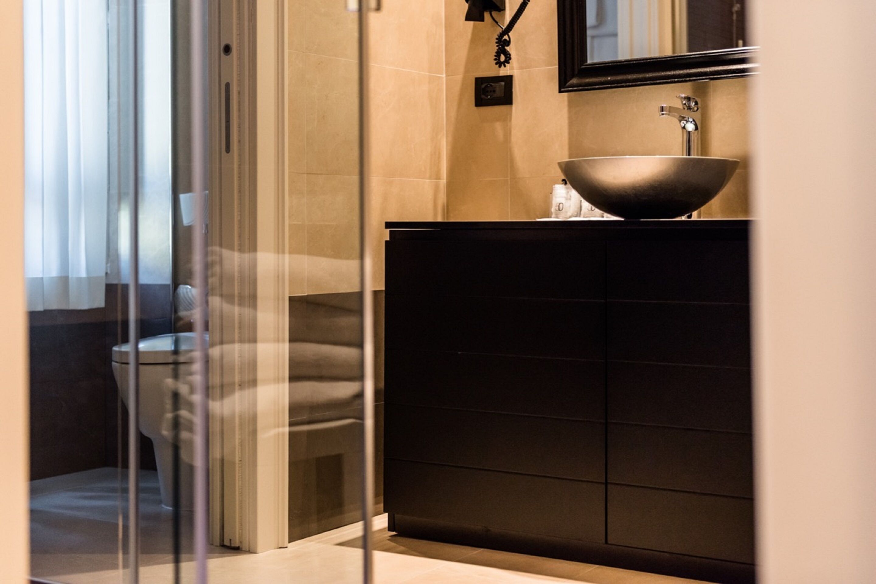 Une salle de bain moderne avec une douche à l’italienne en verre, un meuble-lavabo foncé doté d’un grand évier et un miroir au-dessus de l’évier.