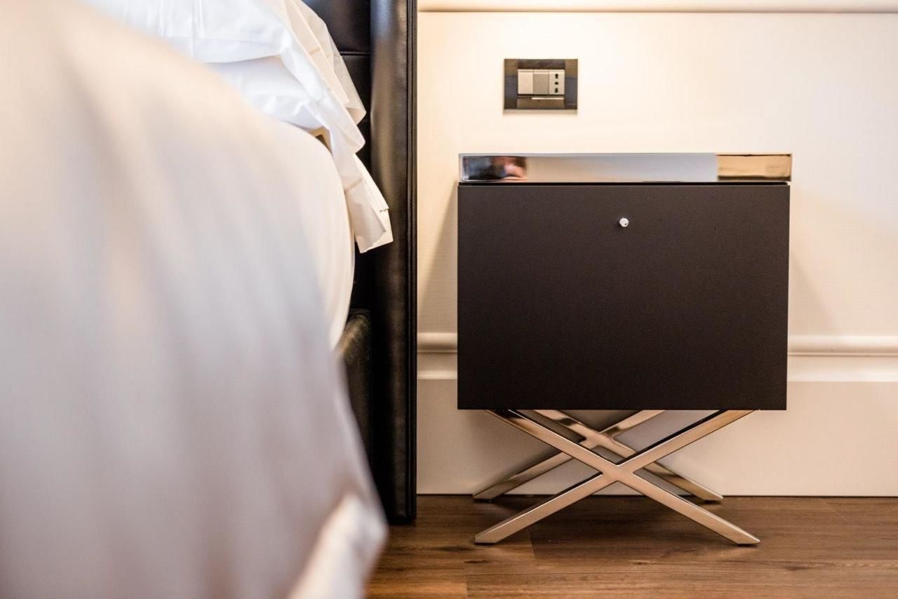 Camera d'albergo moderna con un letto, un comodino nero con televisore a schermo piatto e un interruttore della luce fissato al muro.