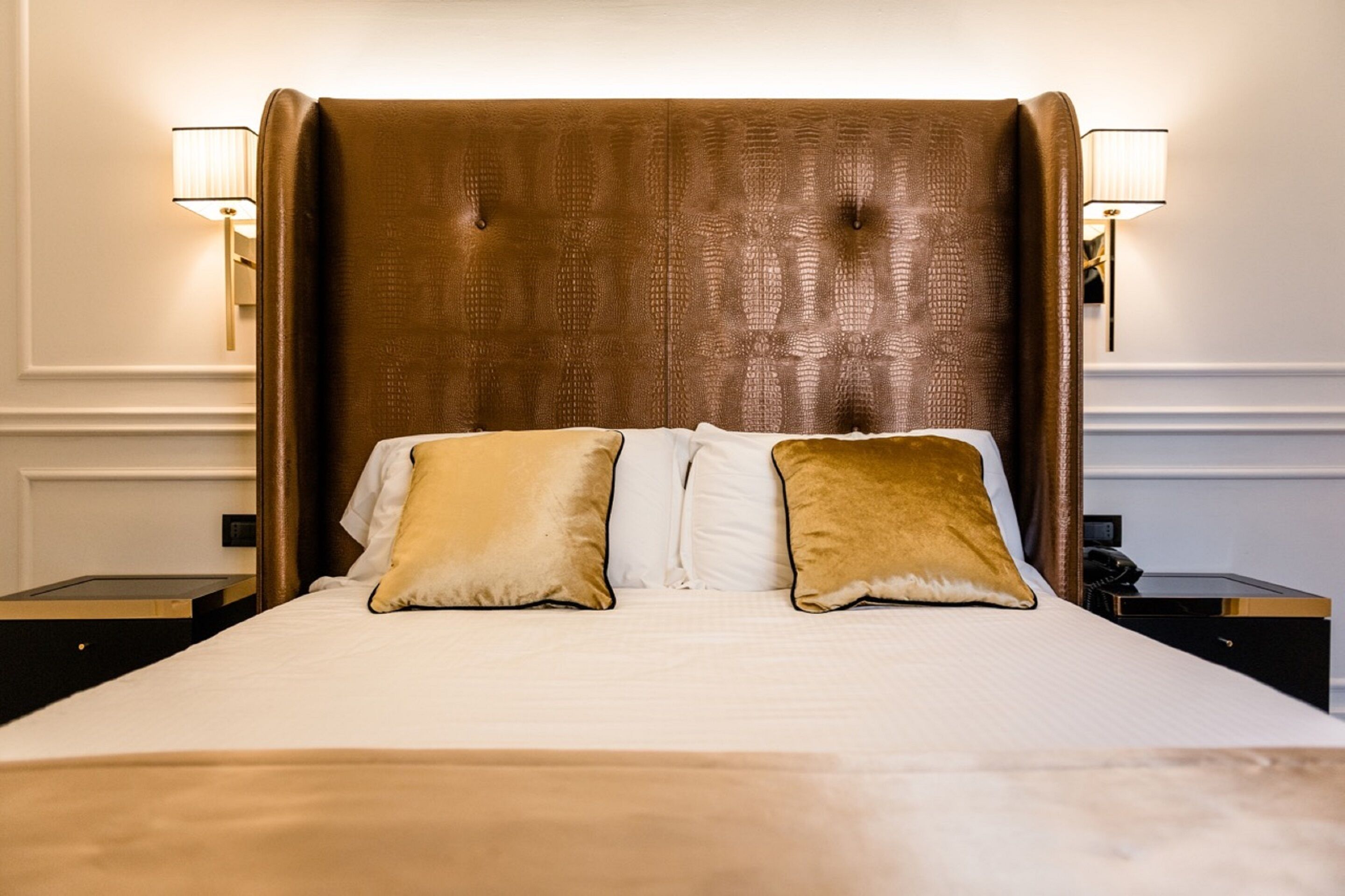 A bed with a tufted headboard, two bedside lamps, and a nightstand with a phone.