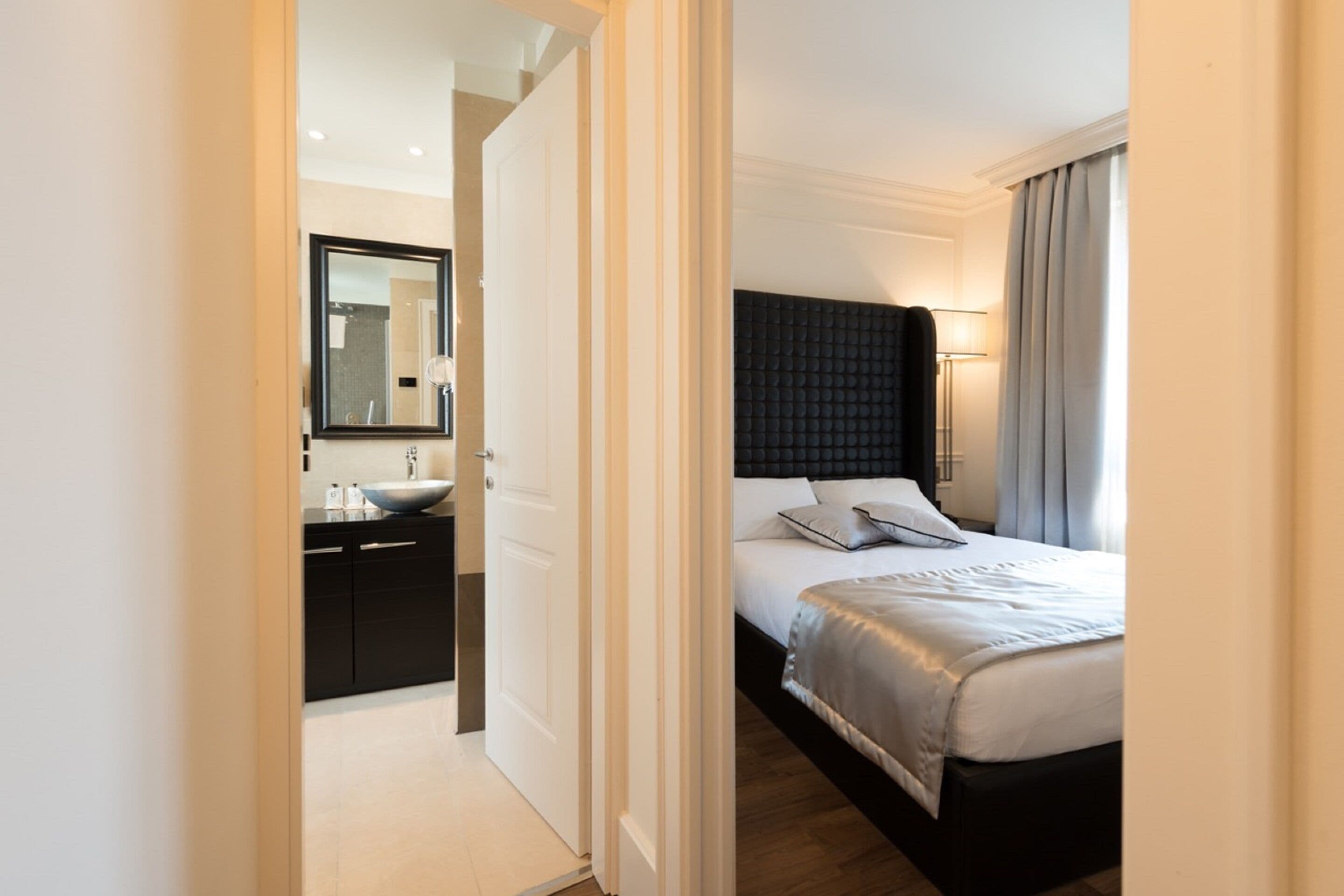 Et hotelværelse med seng, natbord og et badeværelse med vask og spejl.