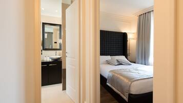 Una habitación de hotel con cama, mesita de noche y baño con lavamanos y espejo.
